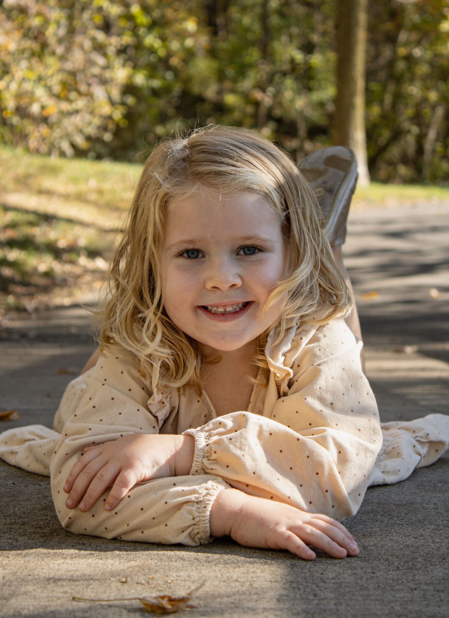 A figure in a beige polka dot dress poses cheerfully on a concrete surface outdoors.