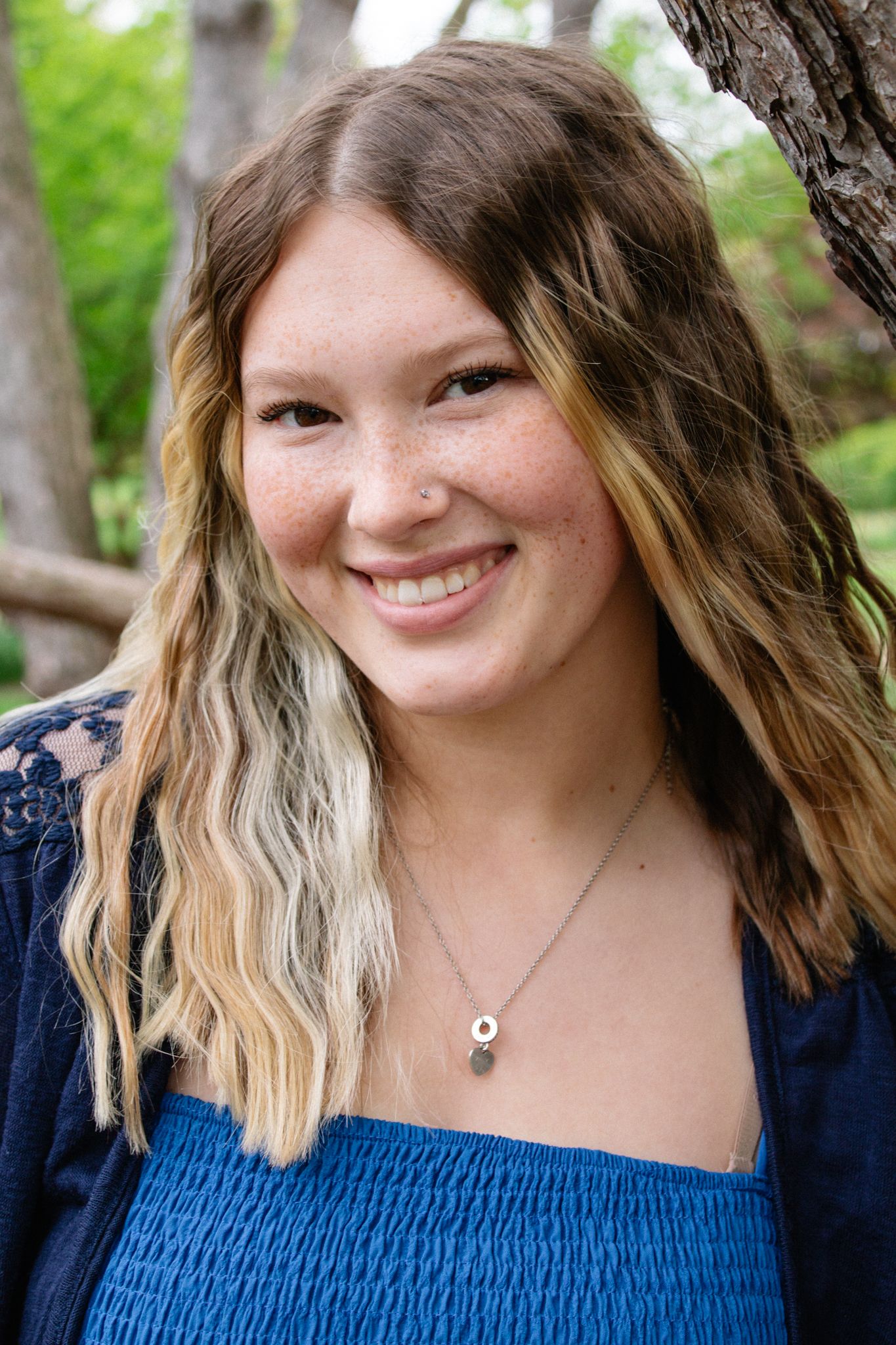 Close-up portrait series in navy blue smocked top against green outdoor backdrop.