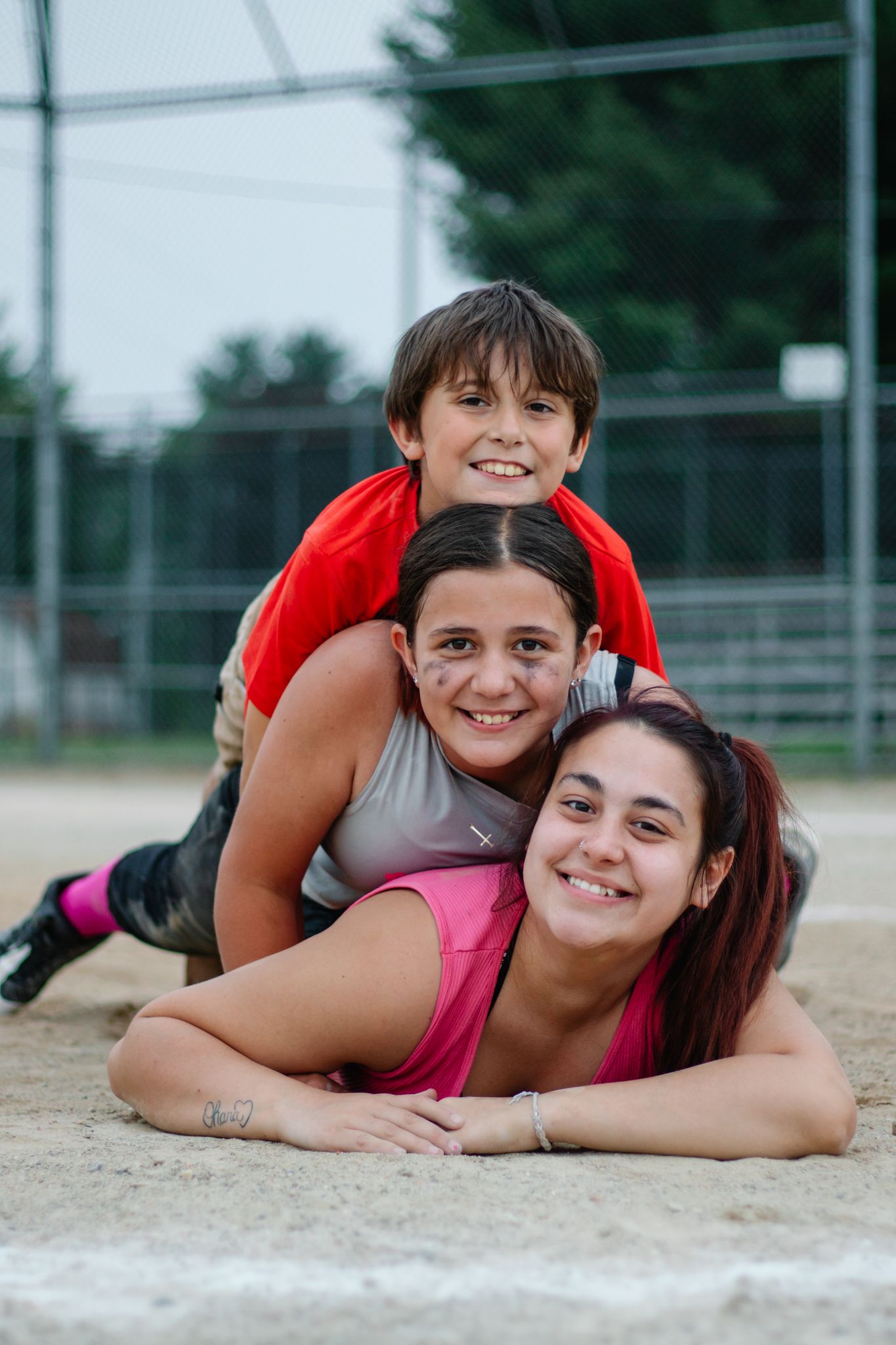 Friends sharing laughs while lying on baseball field during photo shoot.