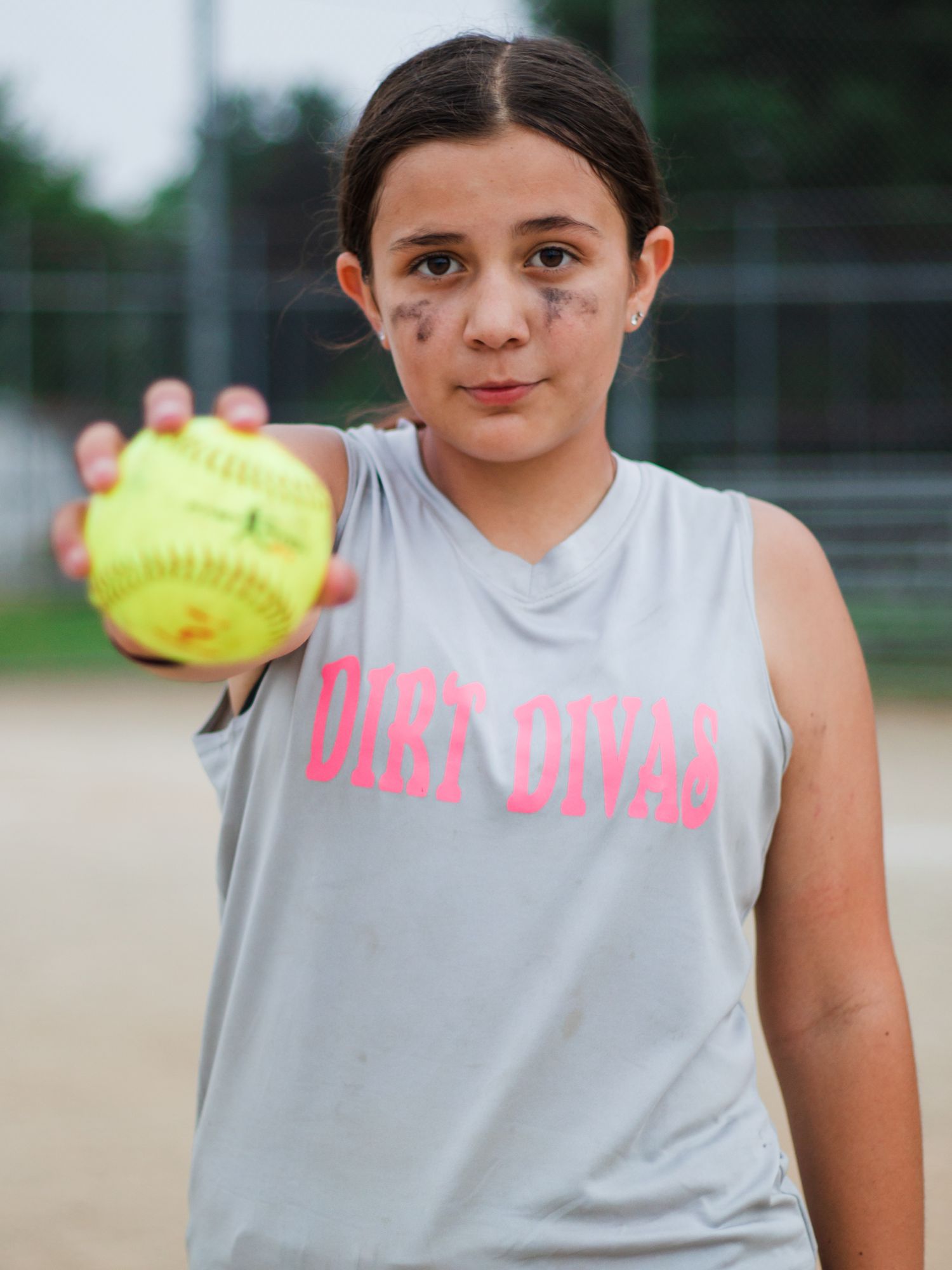 Player in gray sleeveless shirt displays yellow softball on field.