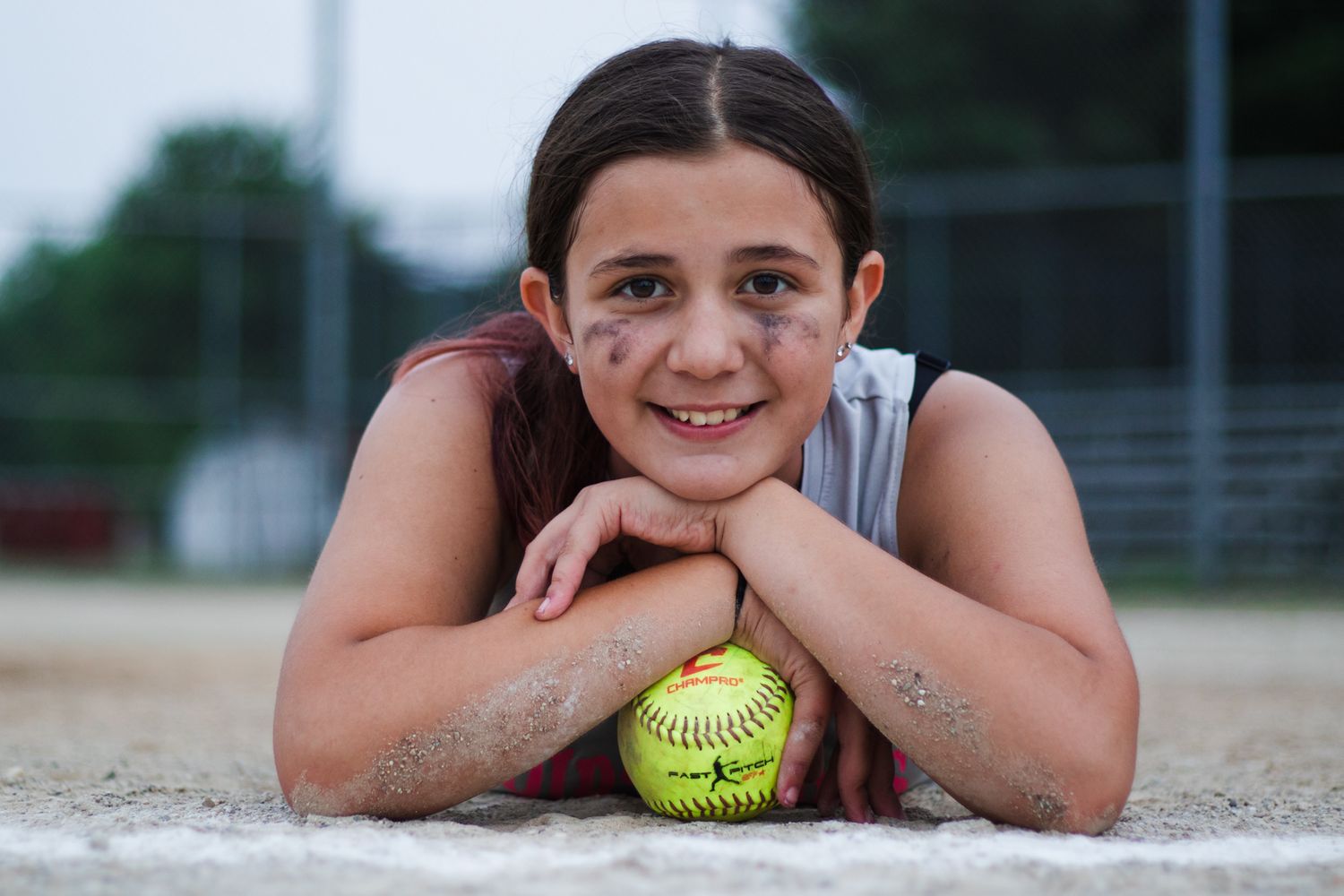 Softball player lying on field with yellow softball resting next to their head smiling at camera.