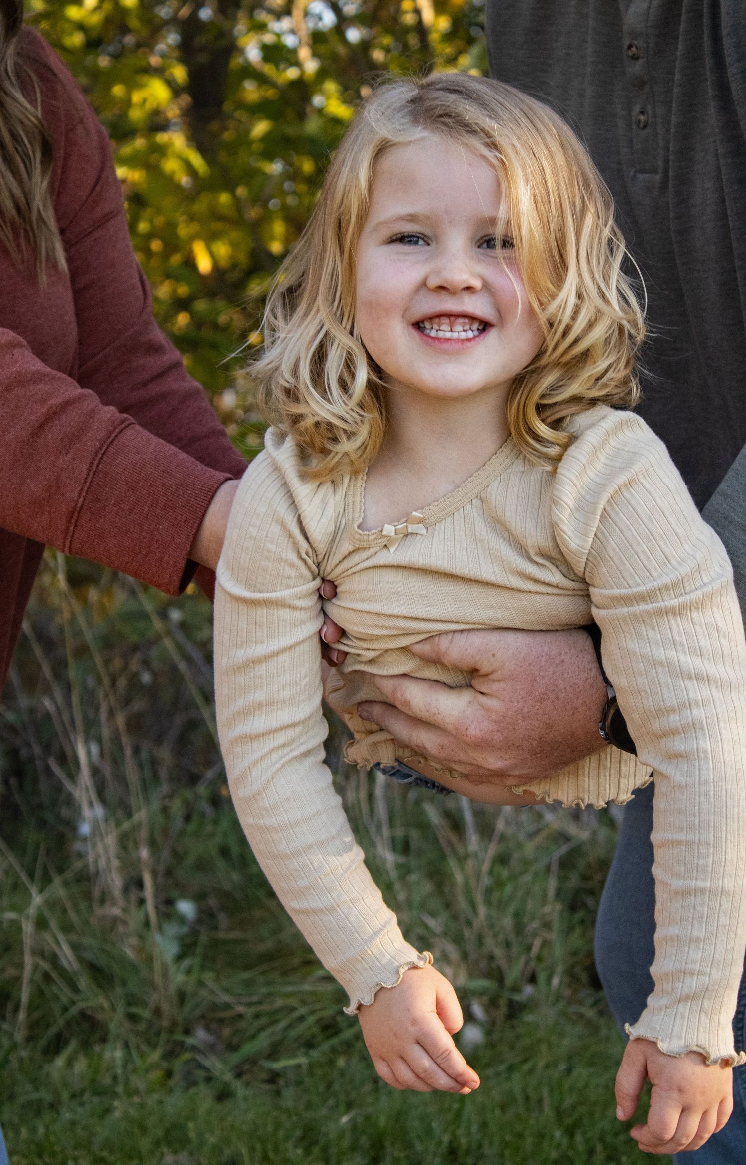 Child in cream sweater plays and laughs during an outdoor autumn photoshoot.