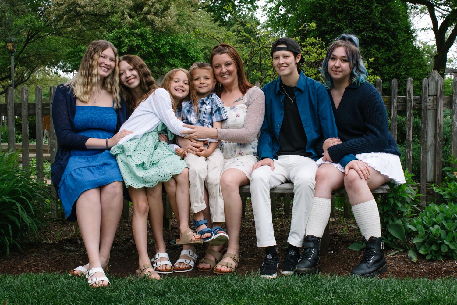 Group sitting casually together on wooden bench in a lush garden setting.