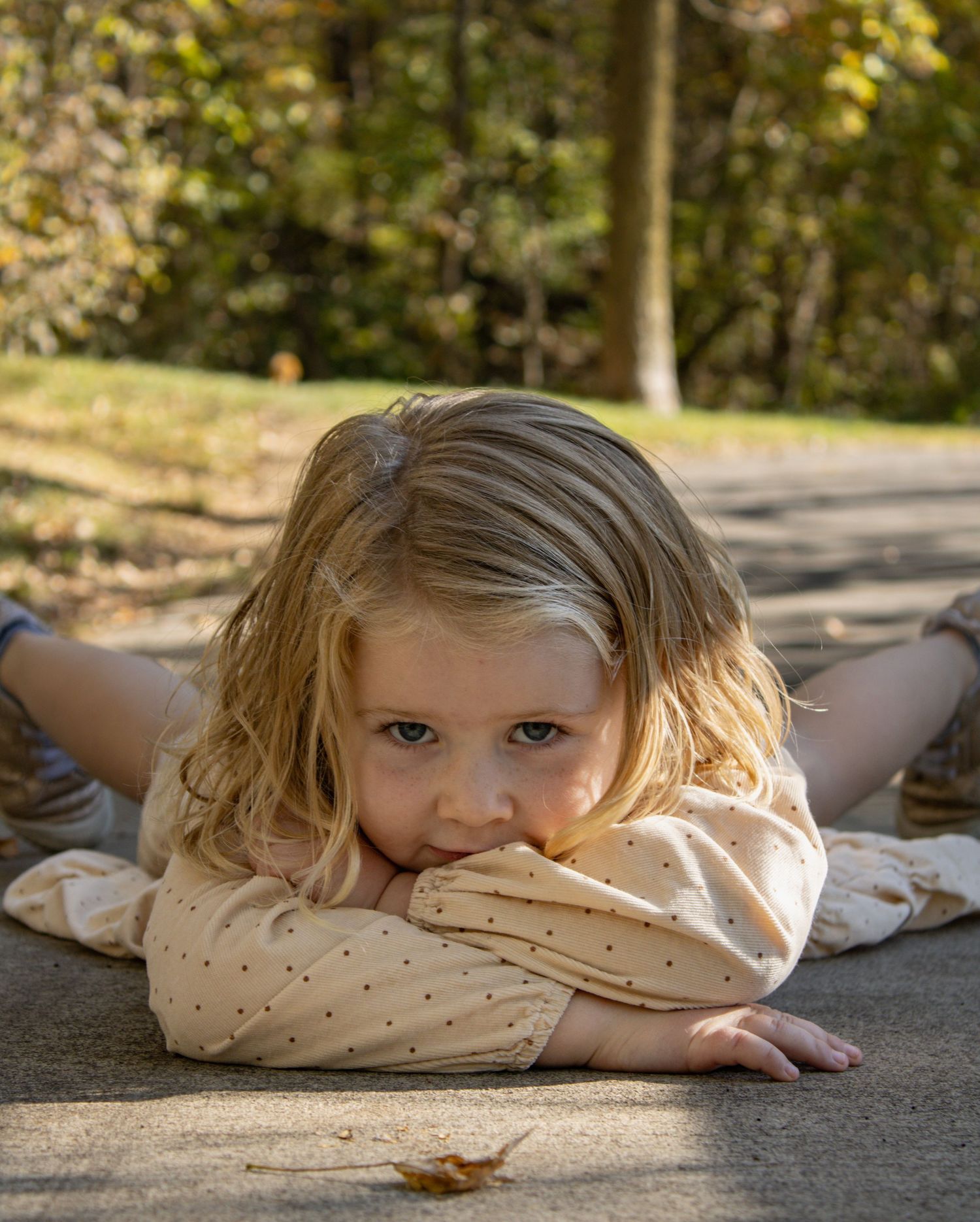 A figure in a polka dot dress lays on concrete in an artistic outdoor pose.