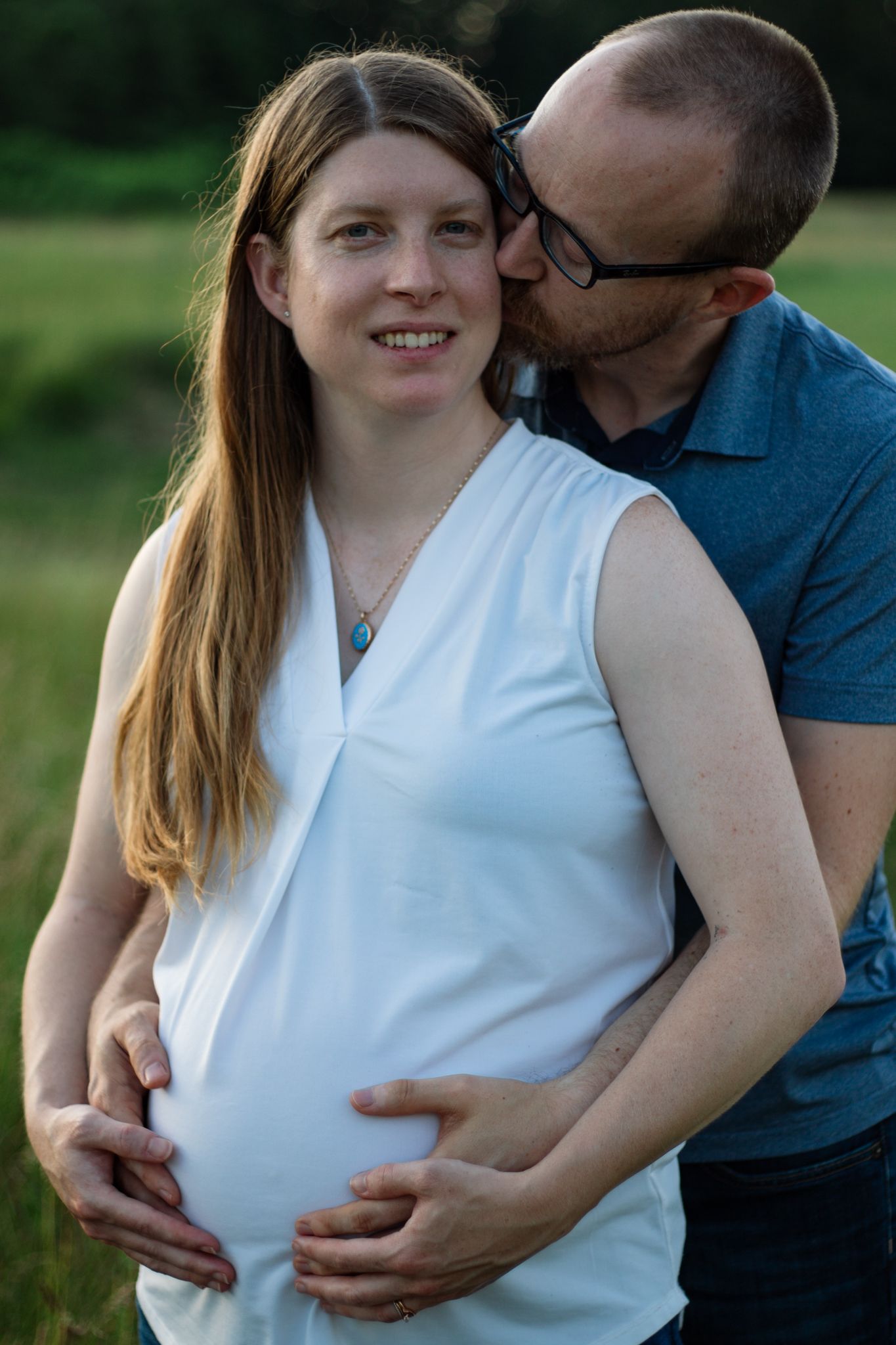 Romantic maternity photo session in white dress outdoors with loving embrace.