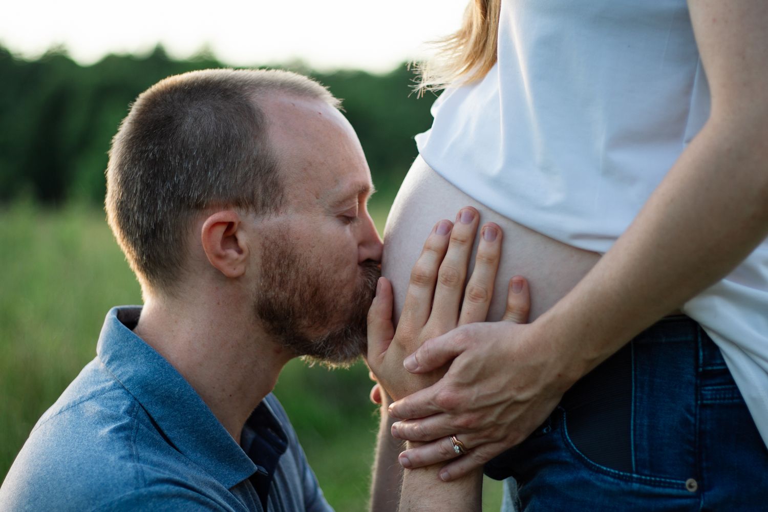 Intimate pregnancy announcement photo in a natural outdoor setting.