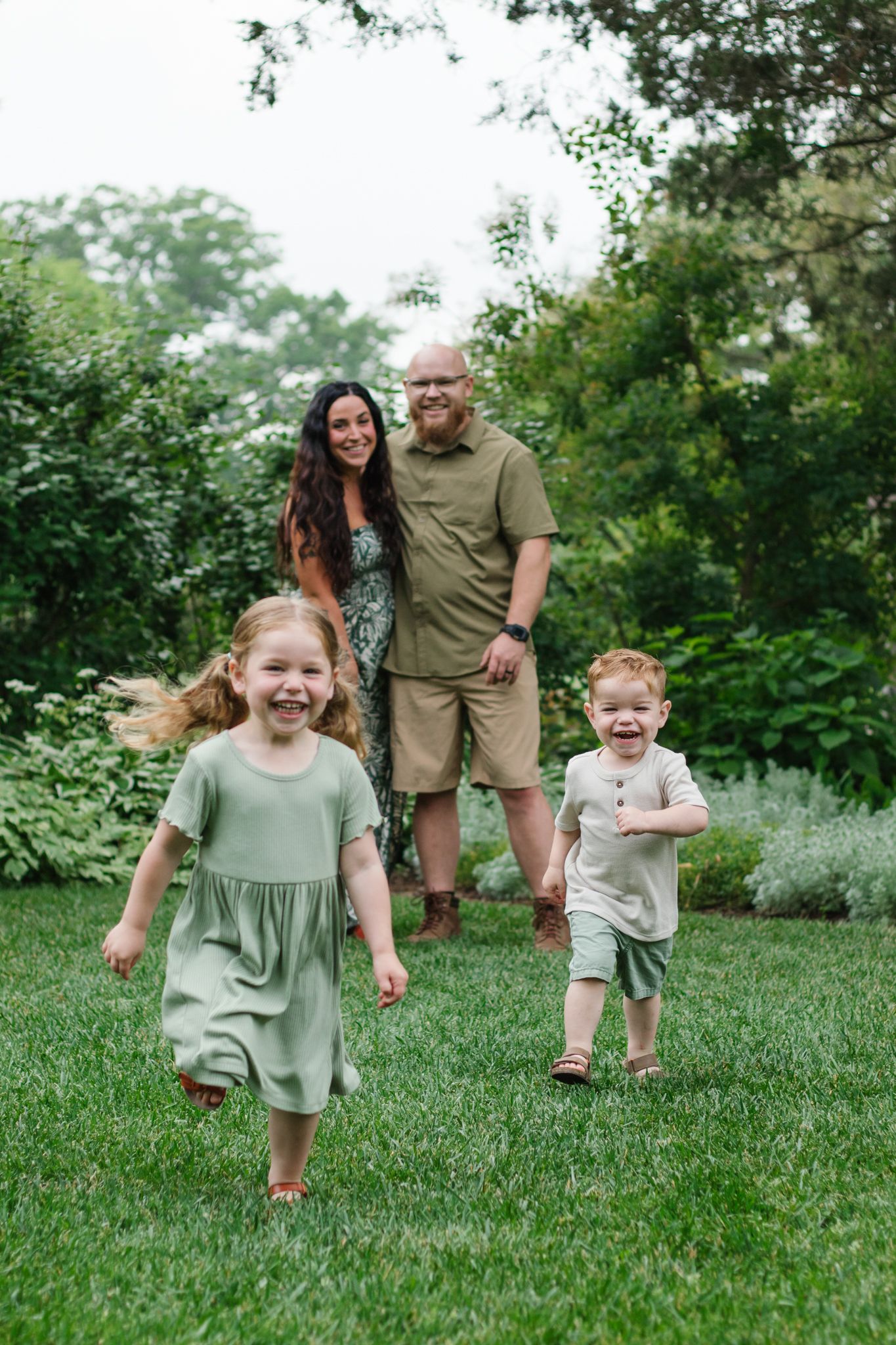 Playful family running and laughing together on green grass in a garden setting.