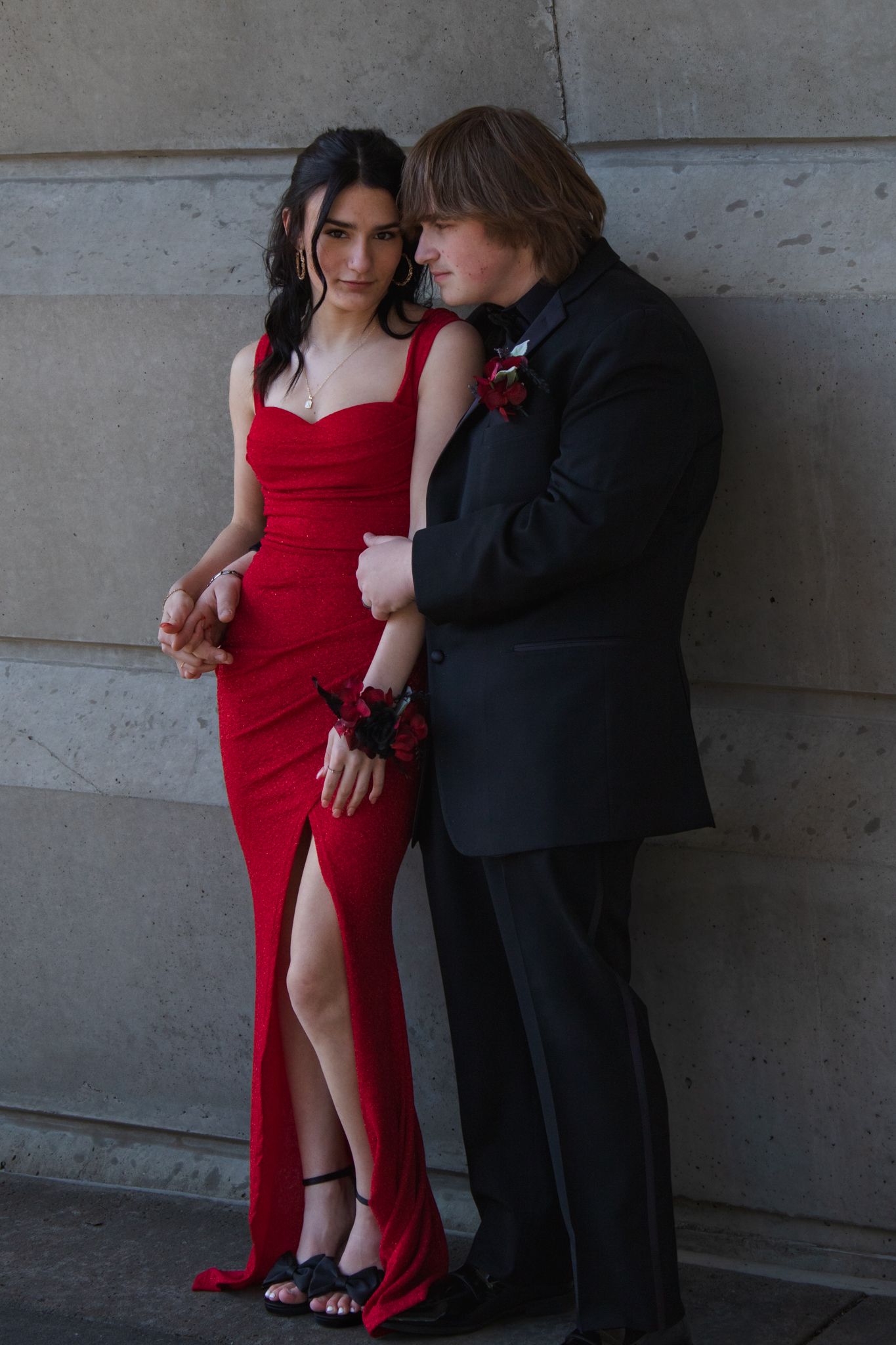 Elegant couple in formal attire pose intimately against stone wall backdrop.