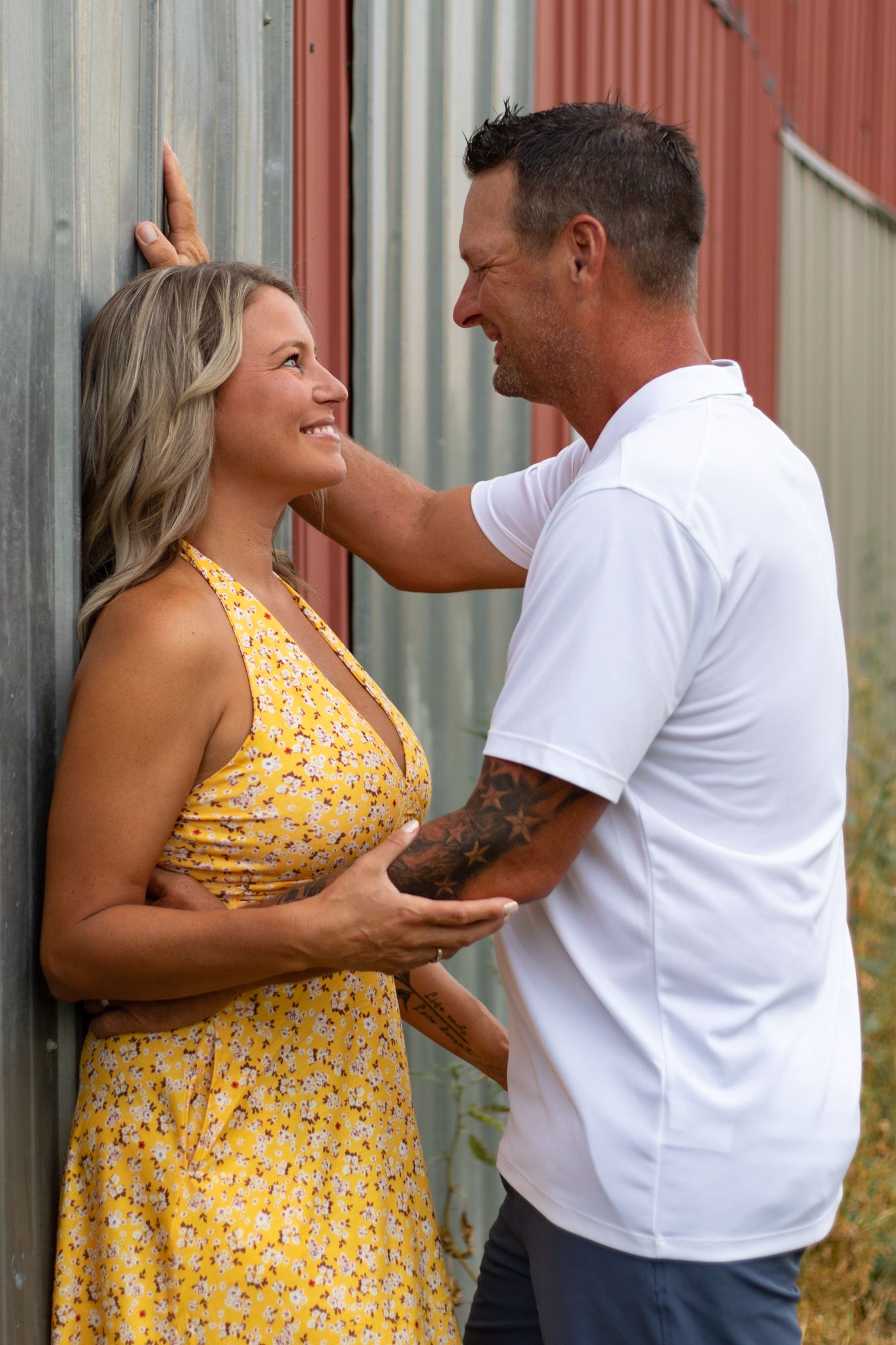 A couple in a yellow dress and white shirt share intimate moments against a rustic backdrop.