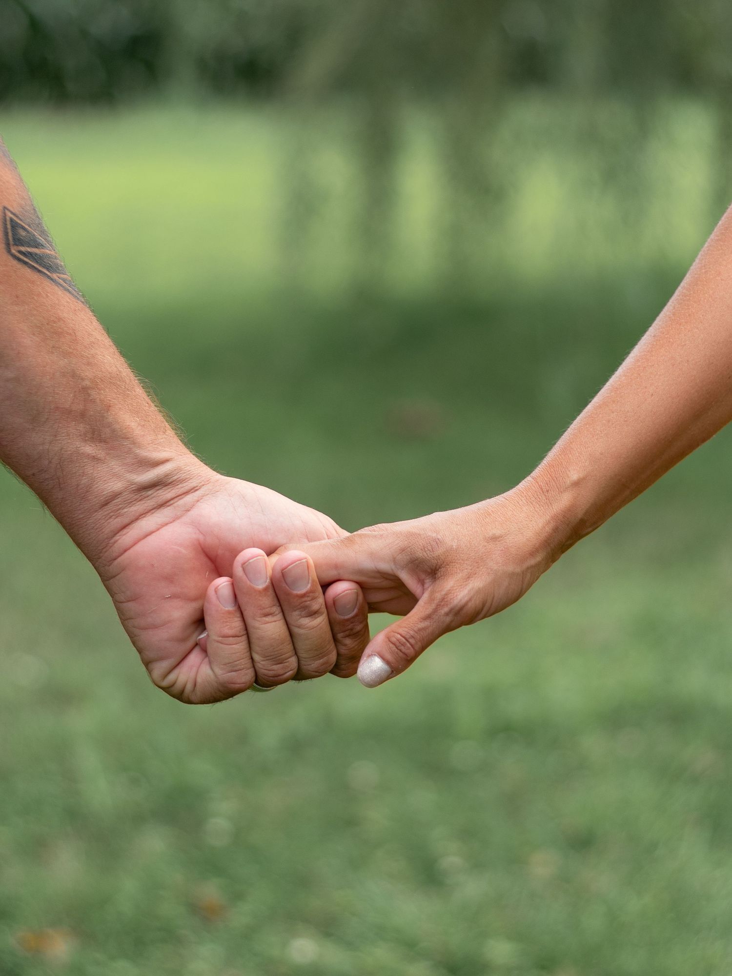 Close-up of hands holding each other tenderly in an outdoor setting with blurred green background.