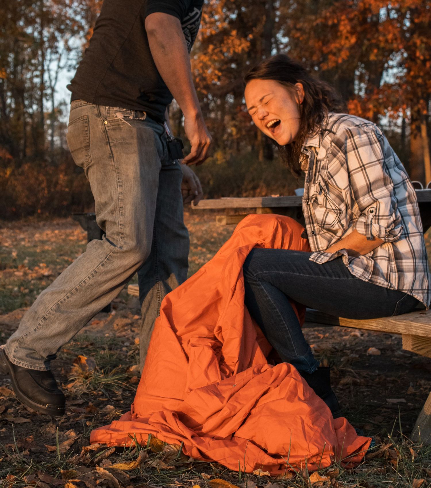 Person laughing while playing with orange blanket outdoors in autumn setting.