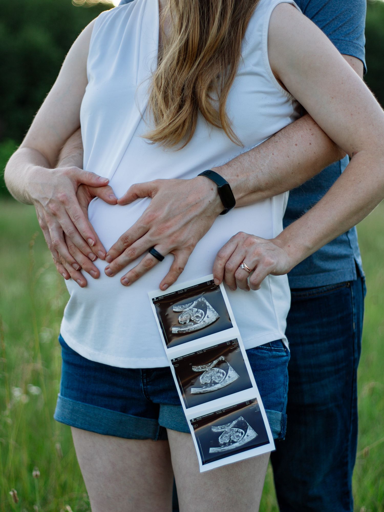 Expectant parents displaying ultrasound images in an outdoor setting.