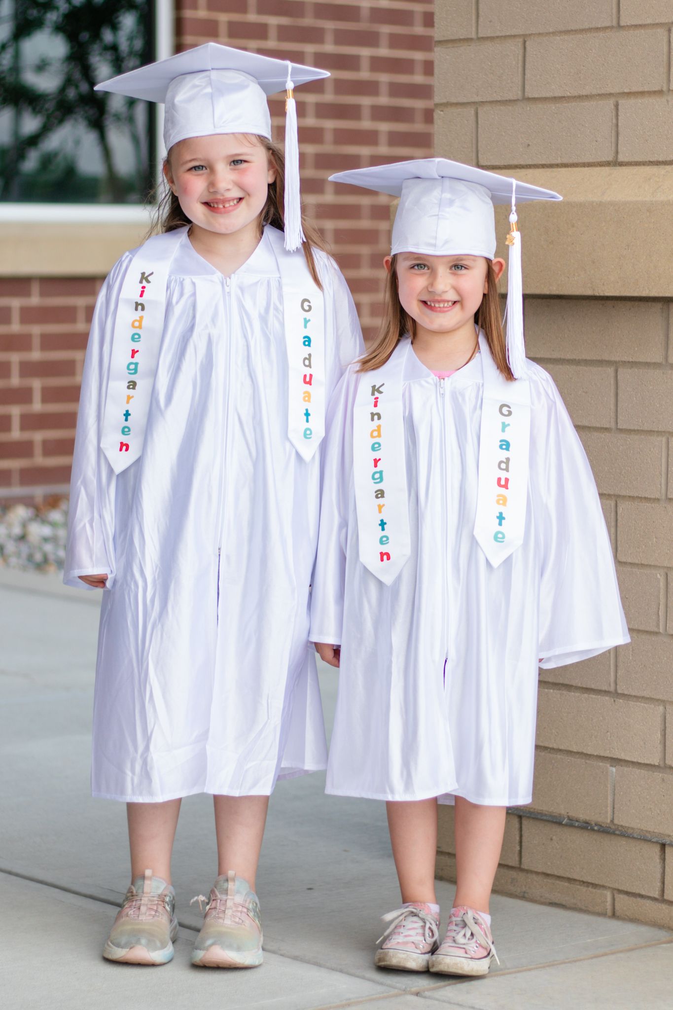 Graduates in traditional white caps and gowns stand together showing their white graduation outfits.