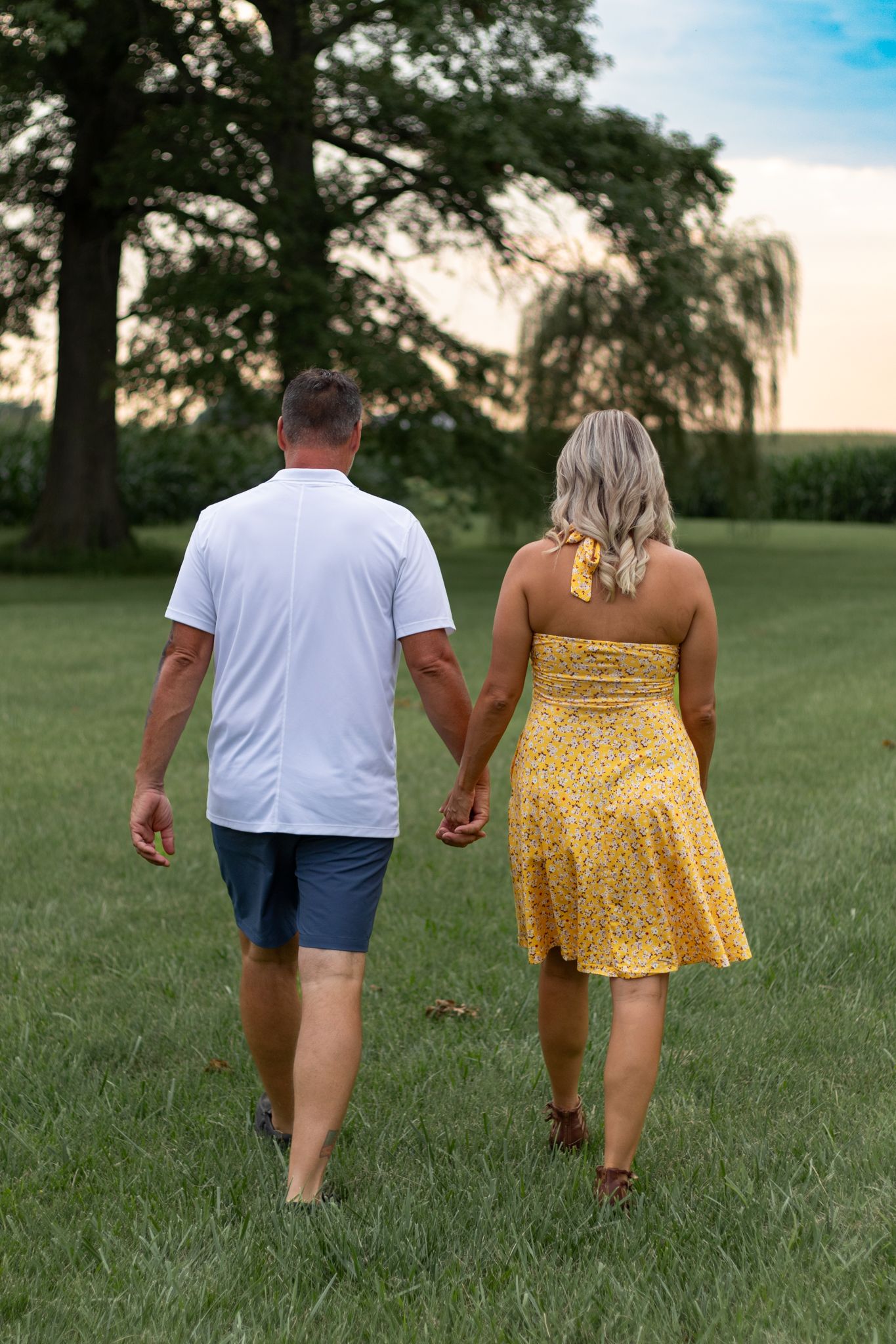 Couple walking away from camera through a grassy field at sunset.