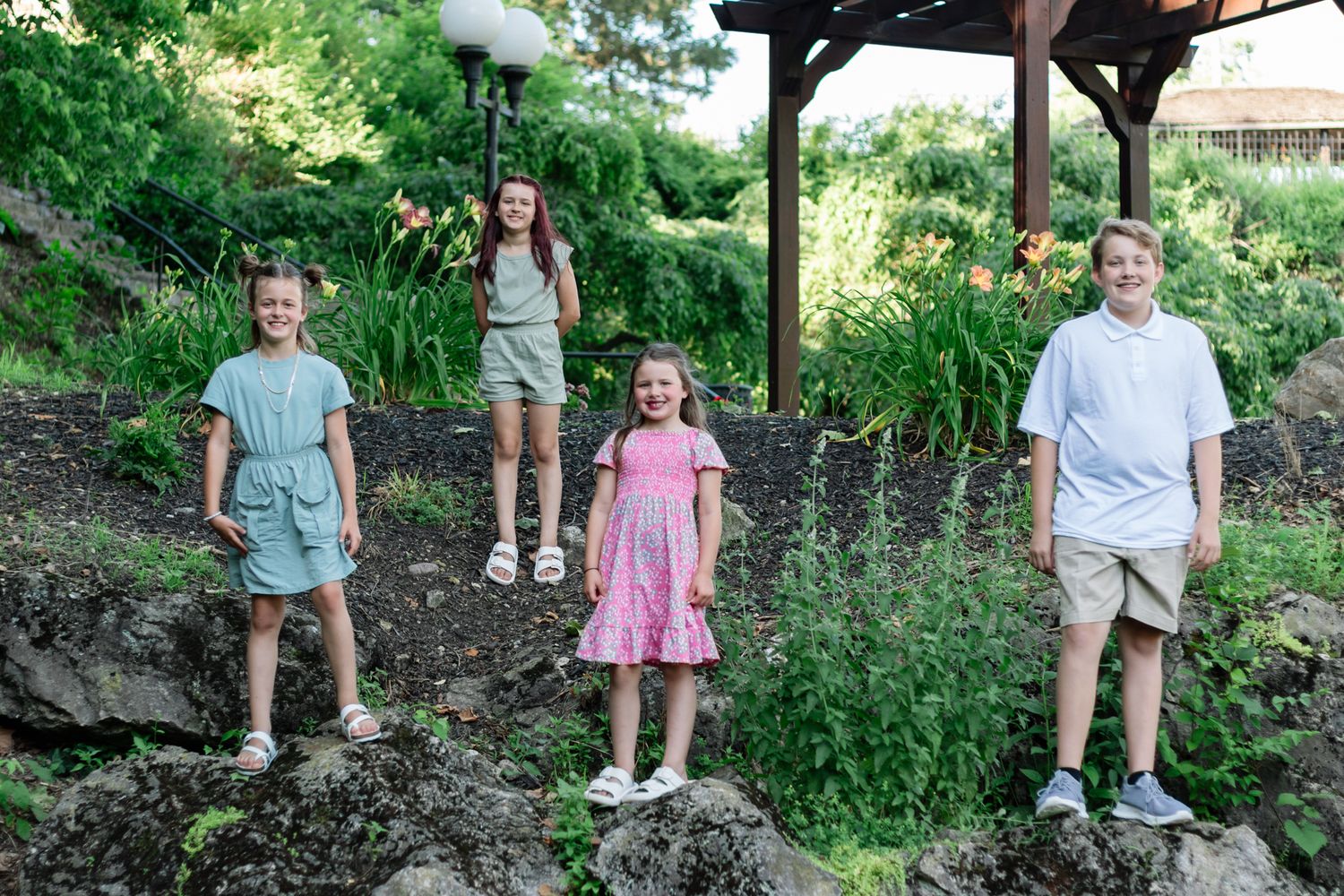 A family group photo session outdoors with everyone wearing coordinated casual summer outfits.