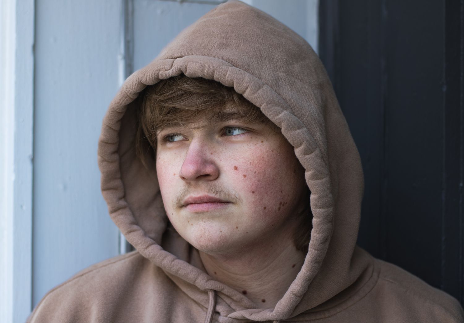 Person in brown hooded jacket shown in profile view against light background.