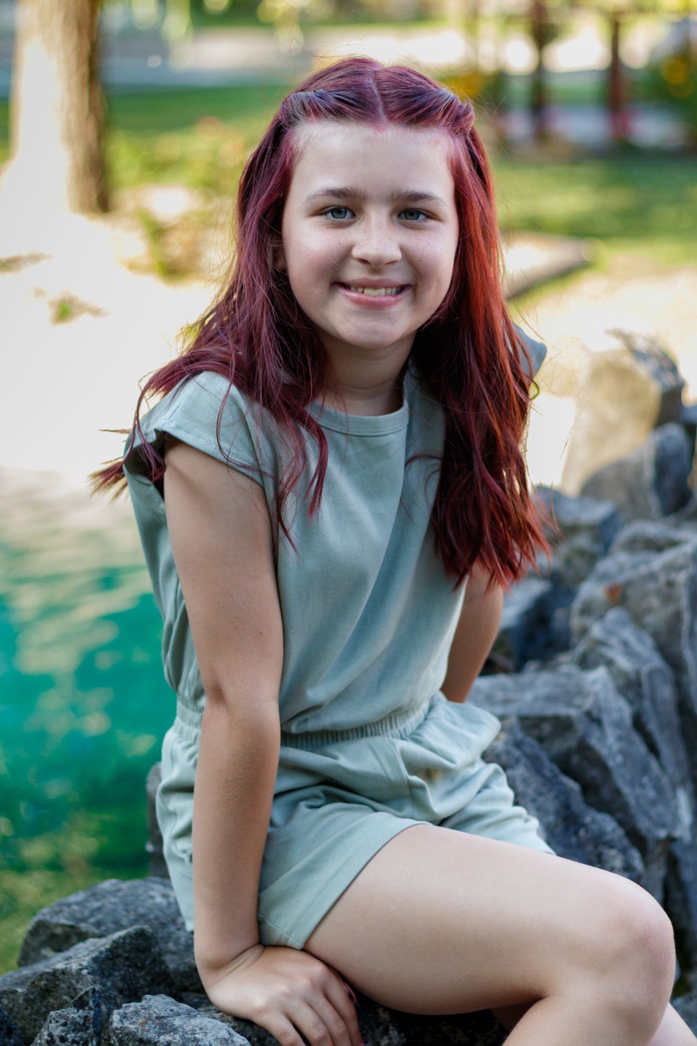 Child in mint green outfit posing on natural rock formation outdoors.
