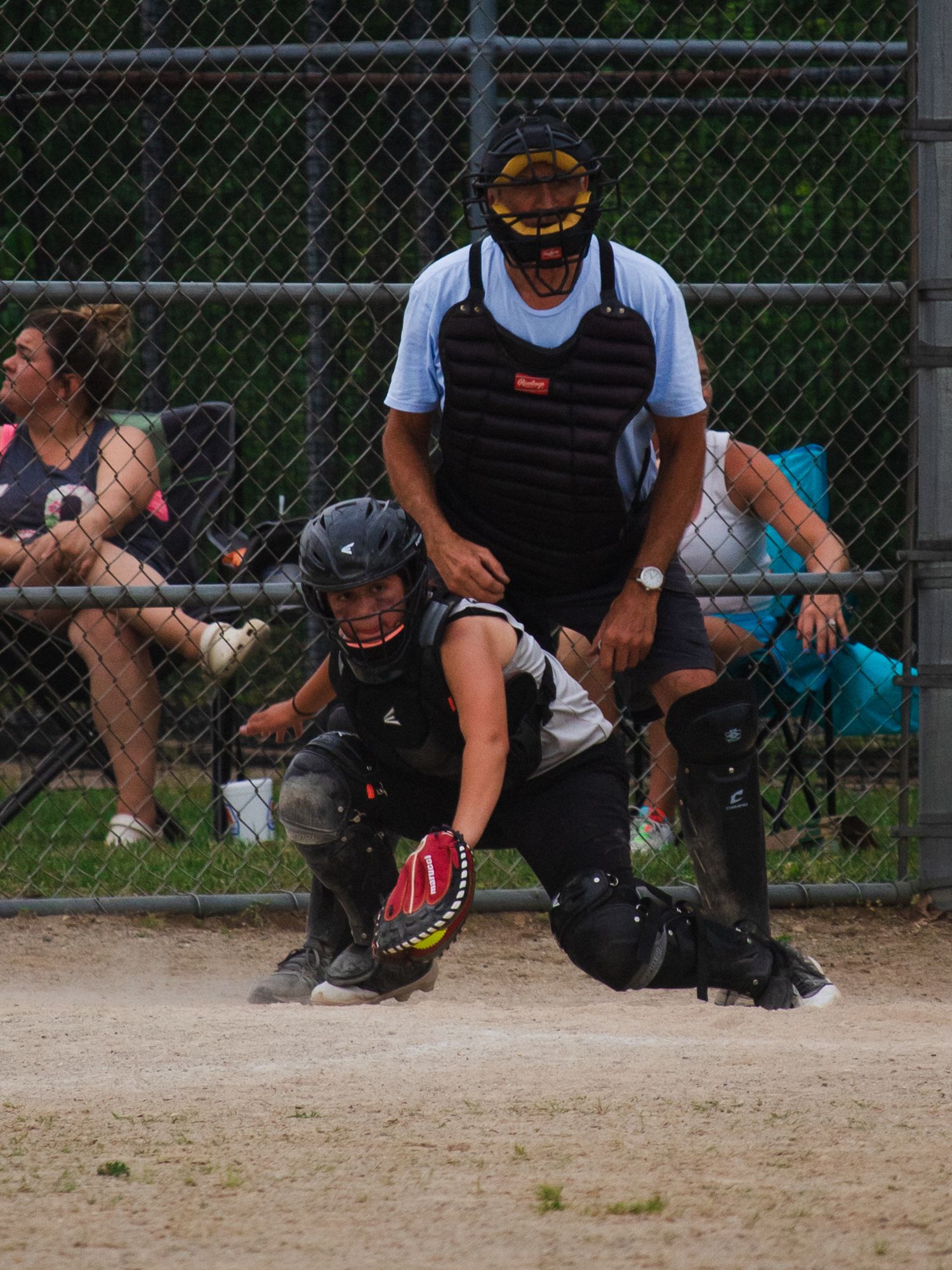Catcher and umpire crouched behind home plate during softball game.
