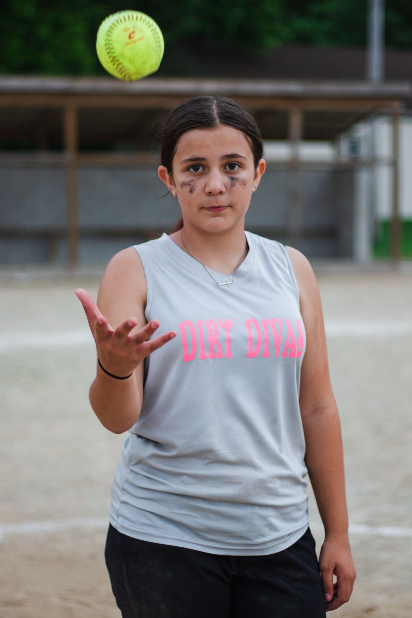 Softball player tosses yellow ball while wearing gray uniform on baseball field.