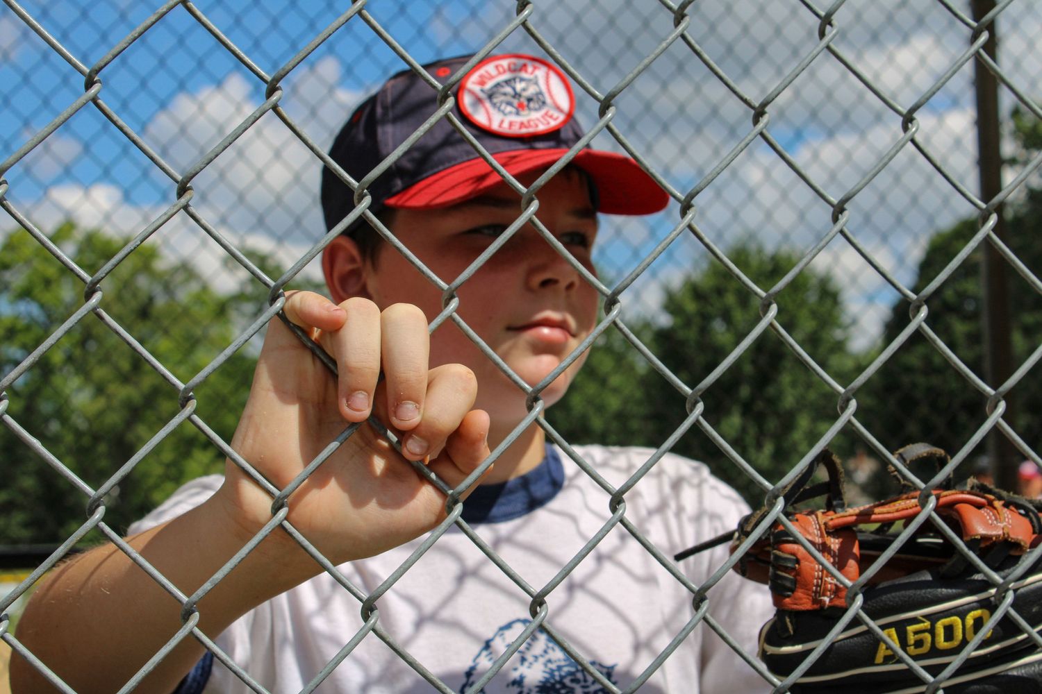Players in baseball uniforms watching through chain link fence at baseball field.
