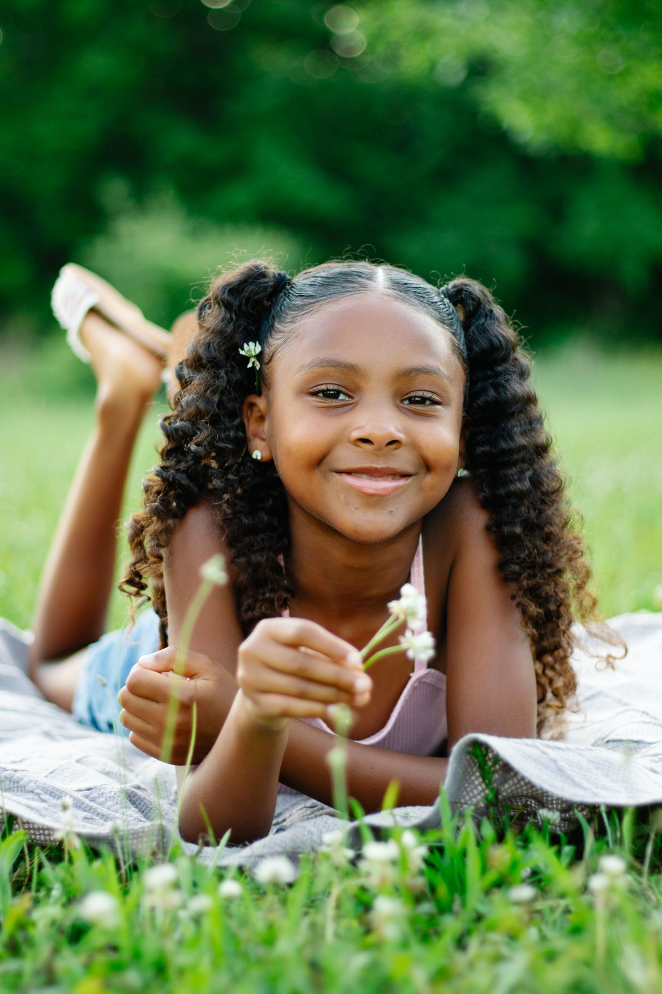 Child laying on blanket in grass field holding flower on sunny day.
