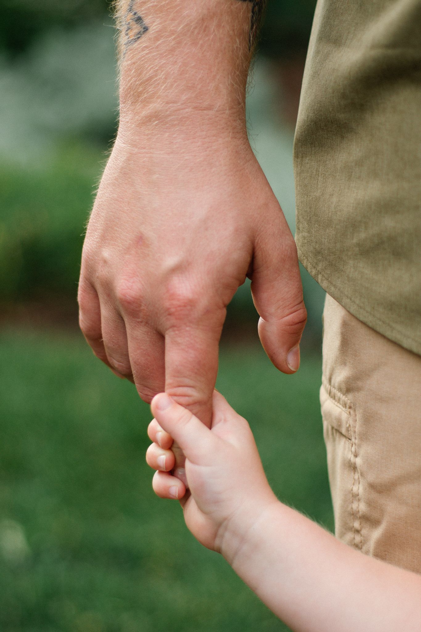 Close-up of parent and child holding hands while walking outdoors.