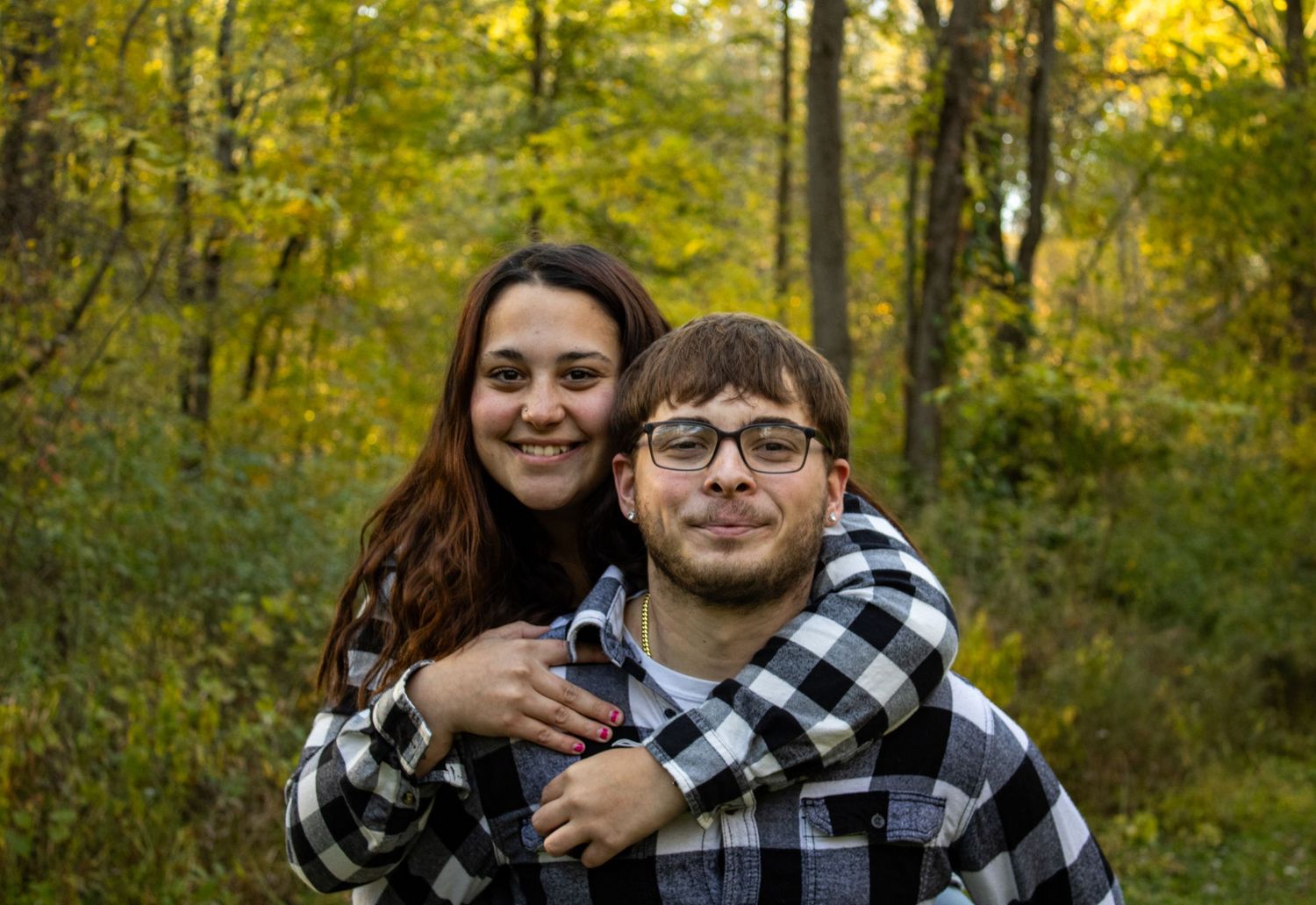 Couple wearing matching plaid shirts embrace in a fall forest setting.