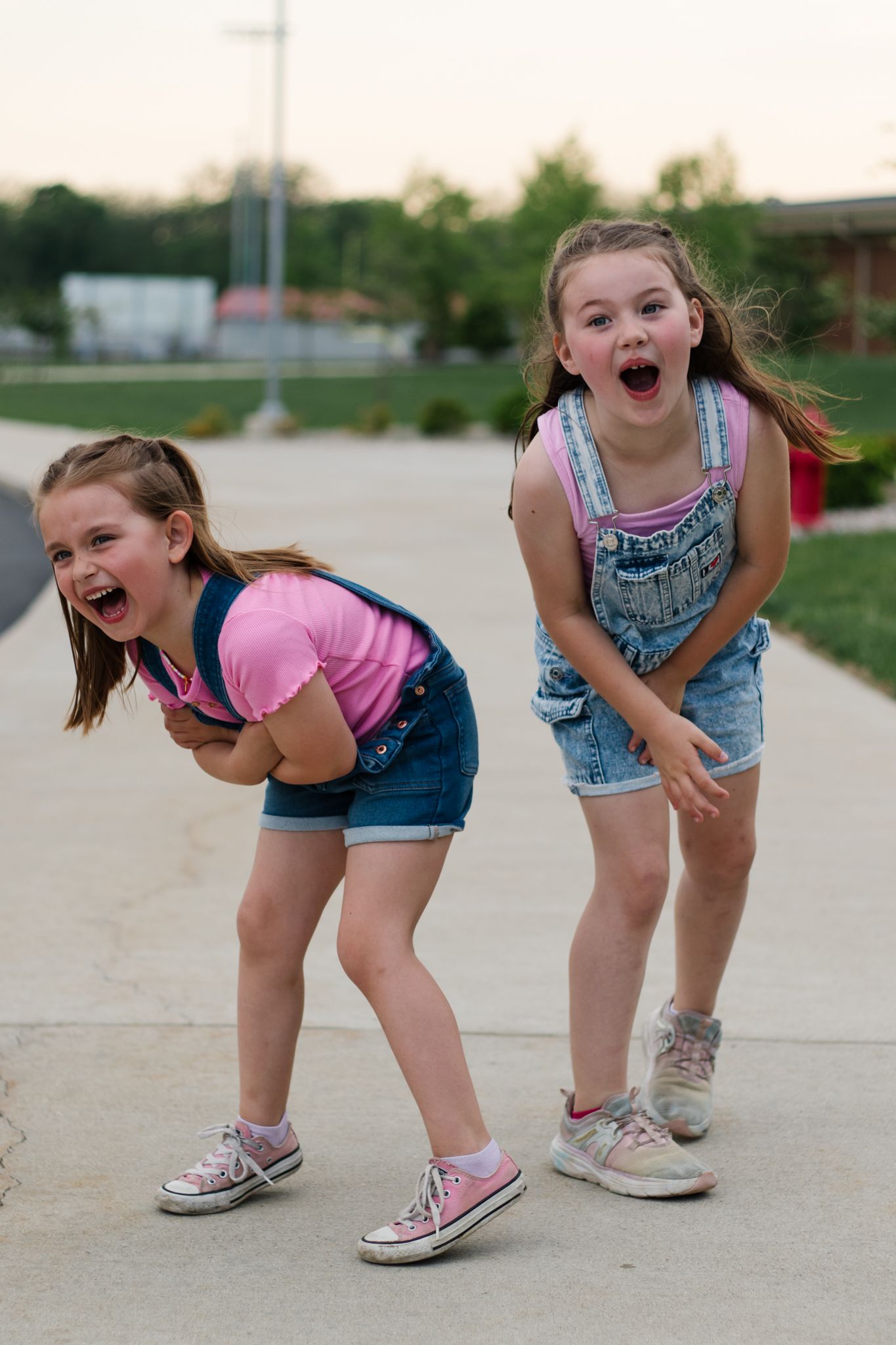 Children in denim overalls laughing and bending forward in a playful pose.
