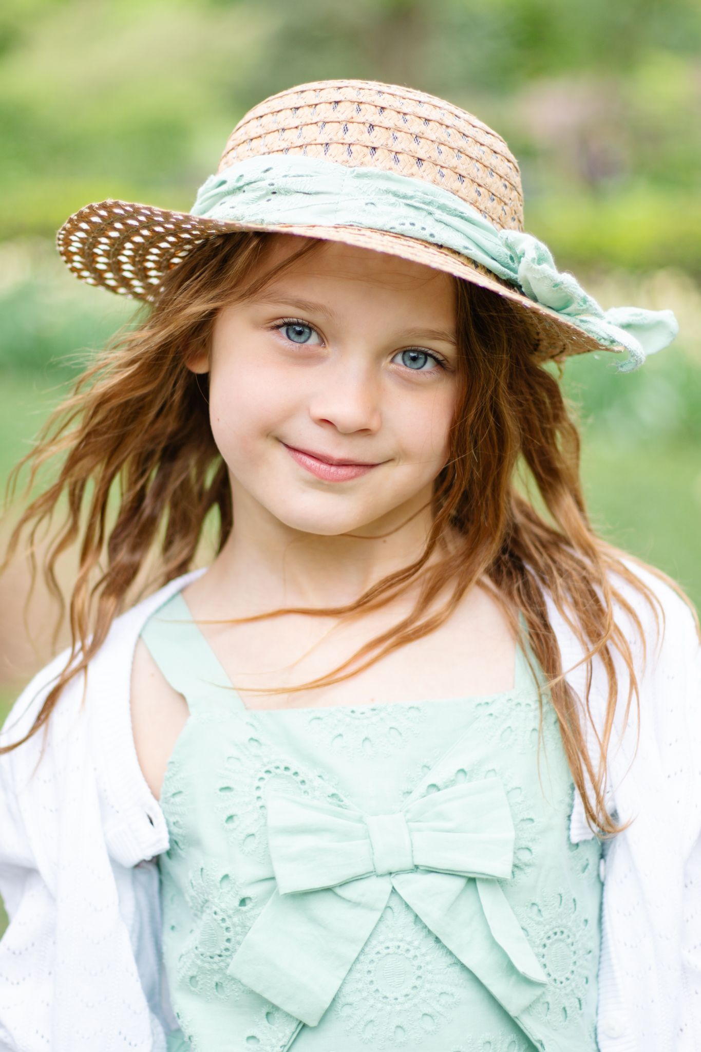 Portrait series in mint green dress with bow detail and straw hat in garden setting.