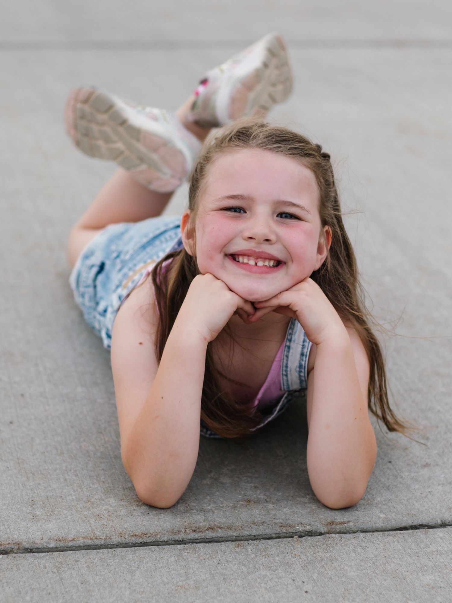 Child in denim lying on concrete with a bright smile.