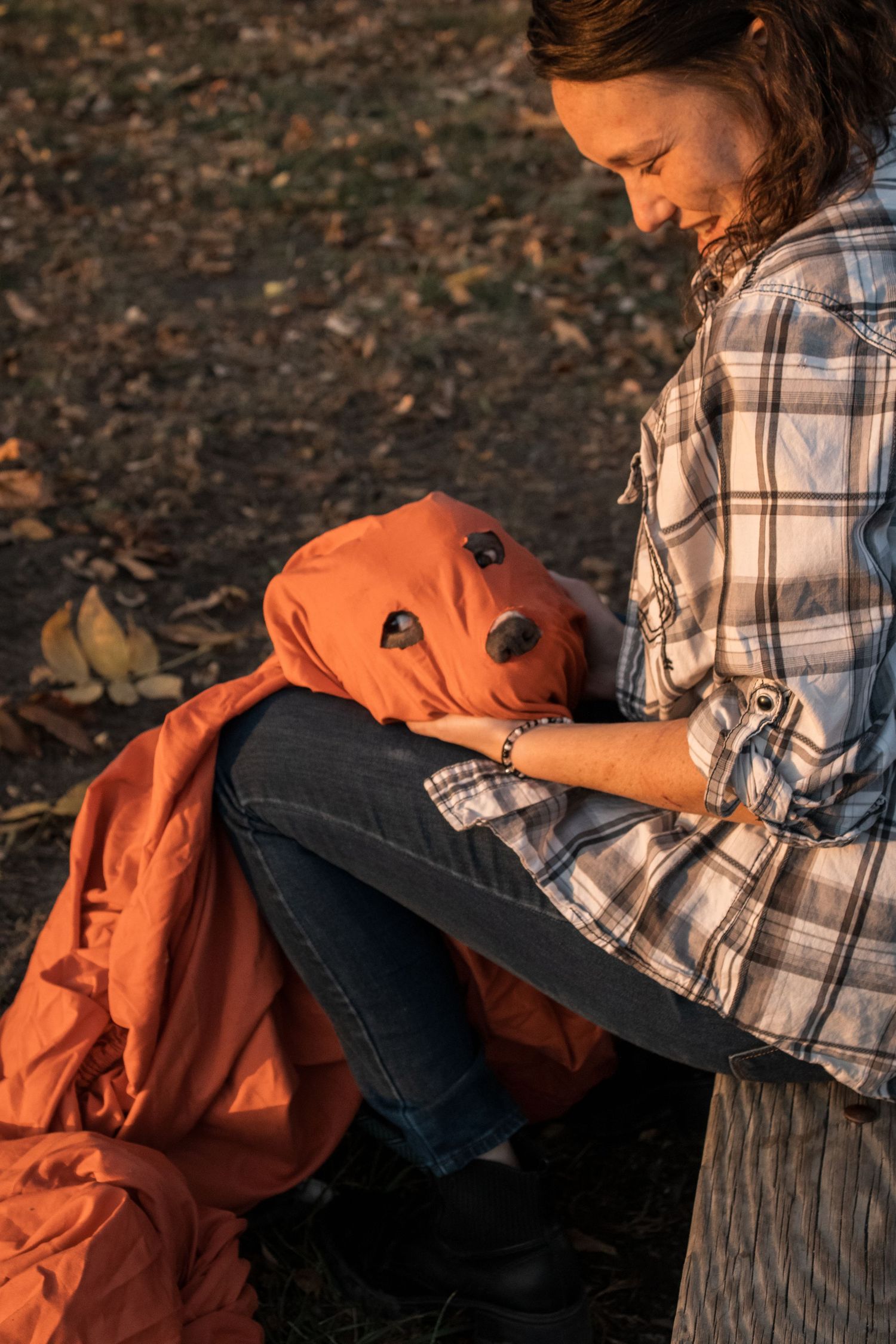 Person handling bright orange fabric material while sitting among autumn leaves.