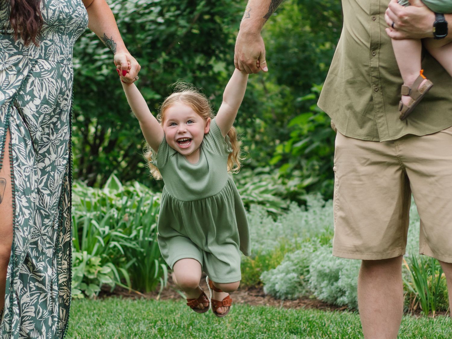 Children playing and posing near stone wall and trees in a lush garden setting.