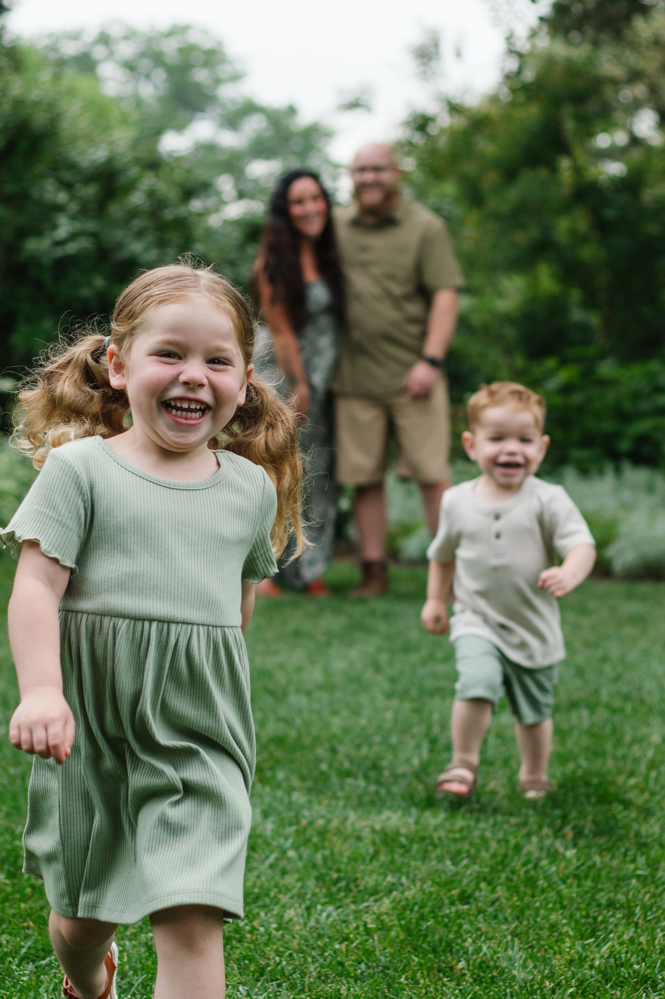 Children running and playing joyfully on green grass with trees in background.