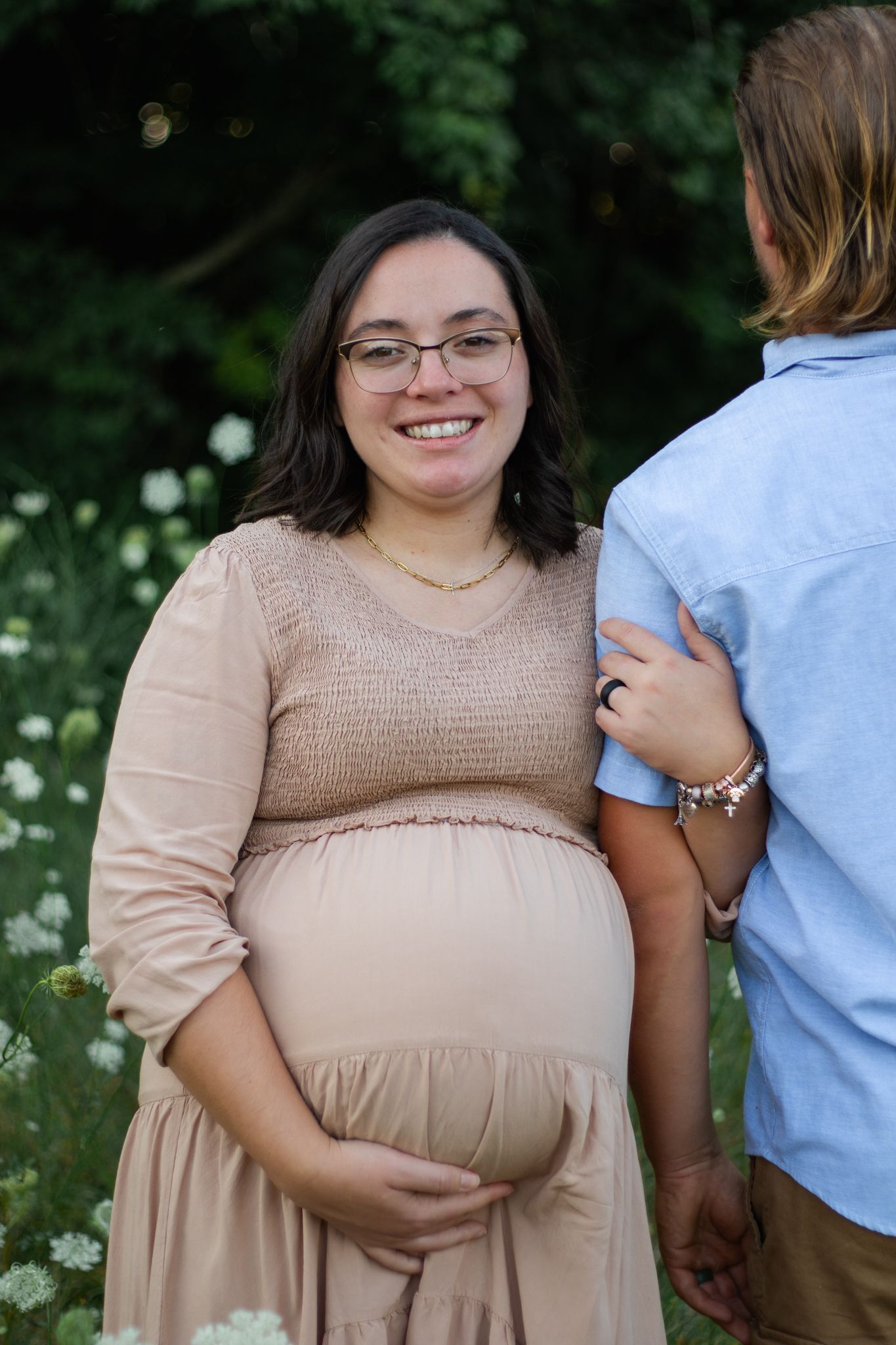 Maternity photoshoot in a field of daisies wearing beige dress.