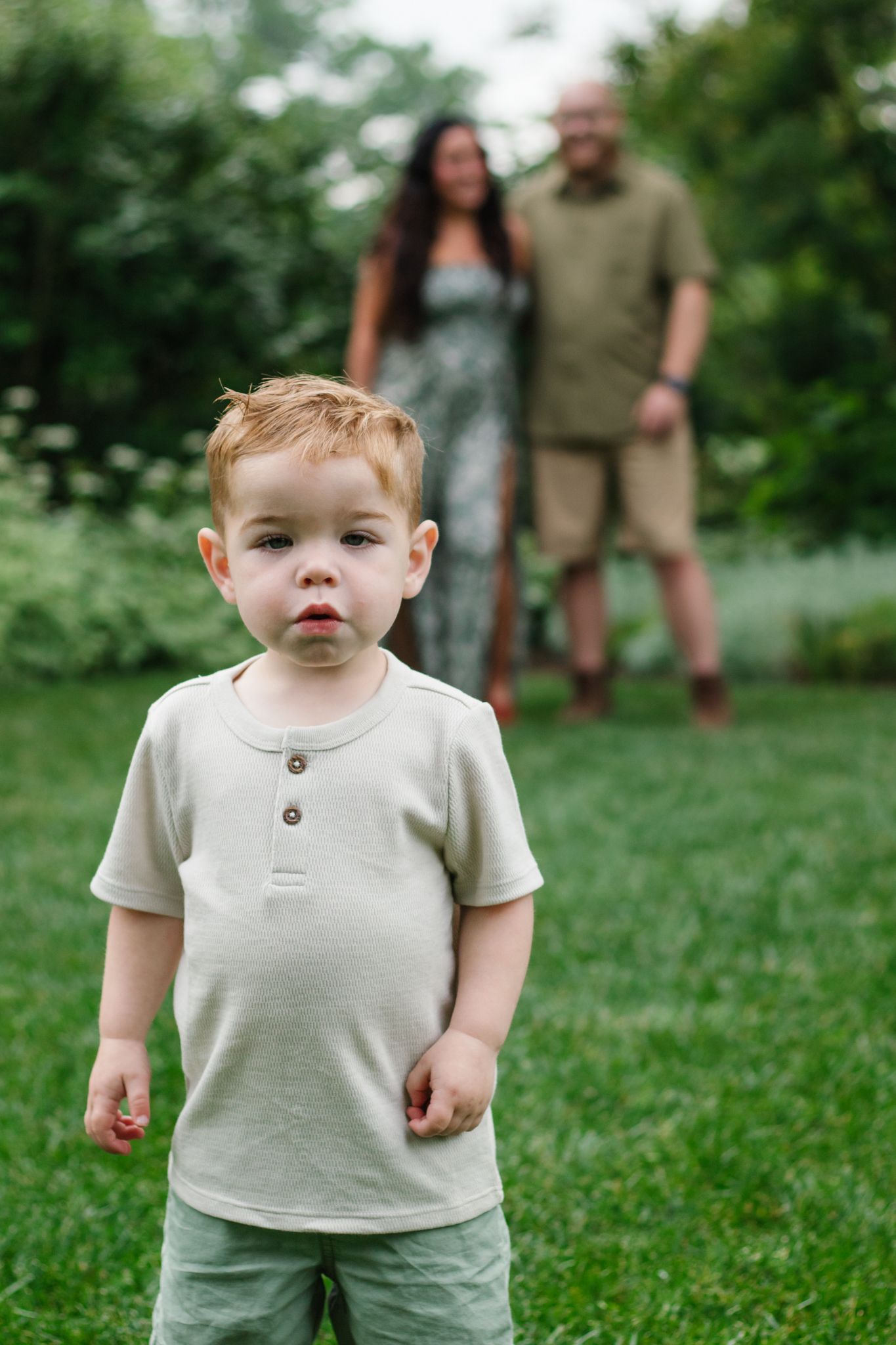 Close up portrait of a toddler in neutral colored clothing against a grassy background.
