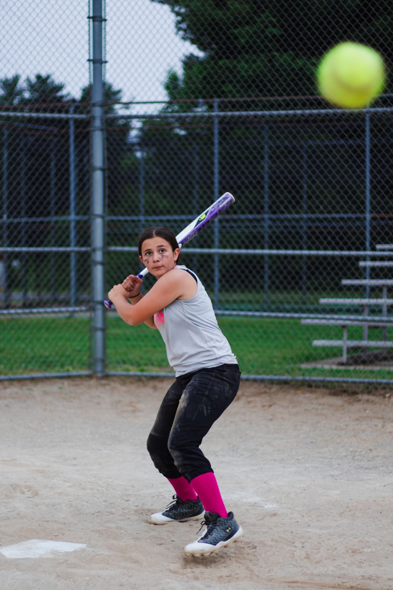 Action sequence of softball batter swinging at pitch on dirt field with chain link fence background.