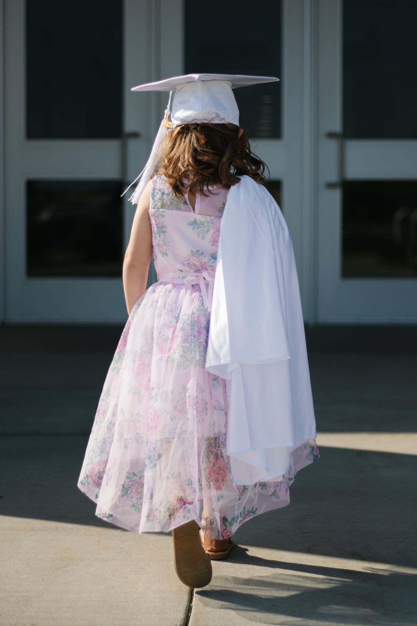 Close-up view of pink floral dress and white graduation cap in sunlight.