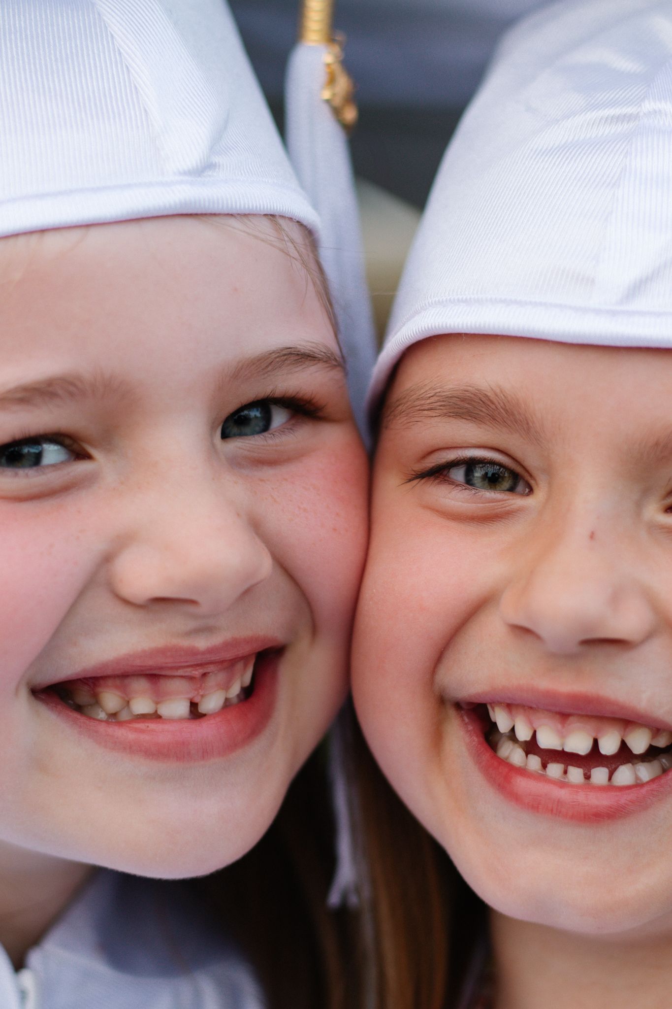 Close up of graduates wearing white caps with tassels as they smile together.