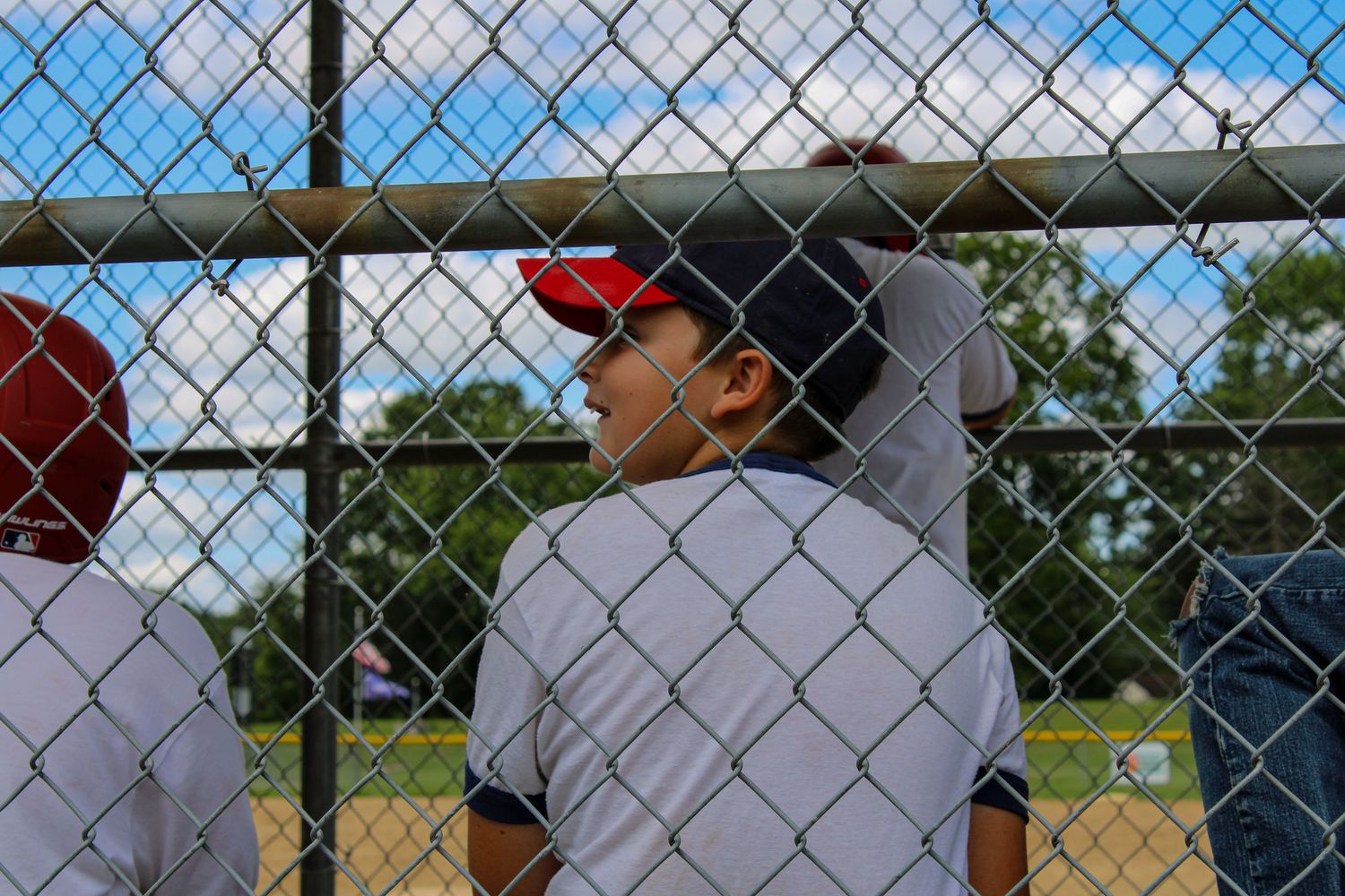 Youth baseball players watching game through chain link fence on sunny afternoon.