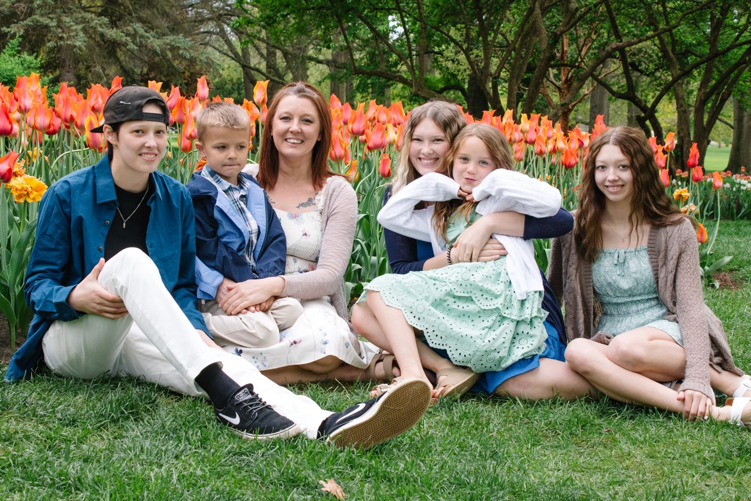 Family sitting together on grass with orange tulips blooming in garden background.