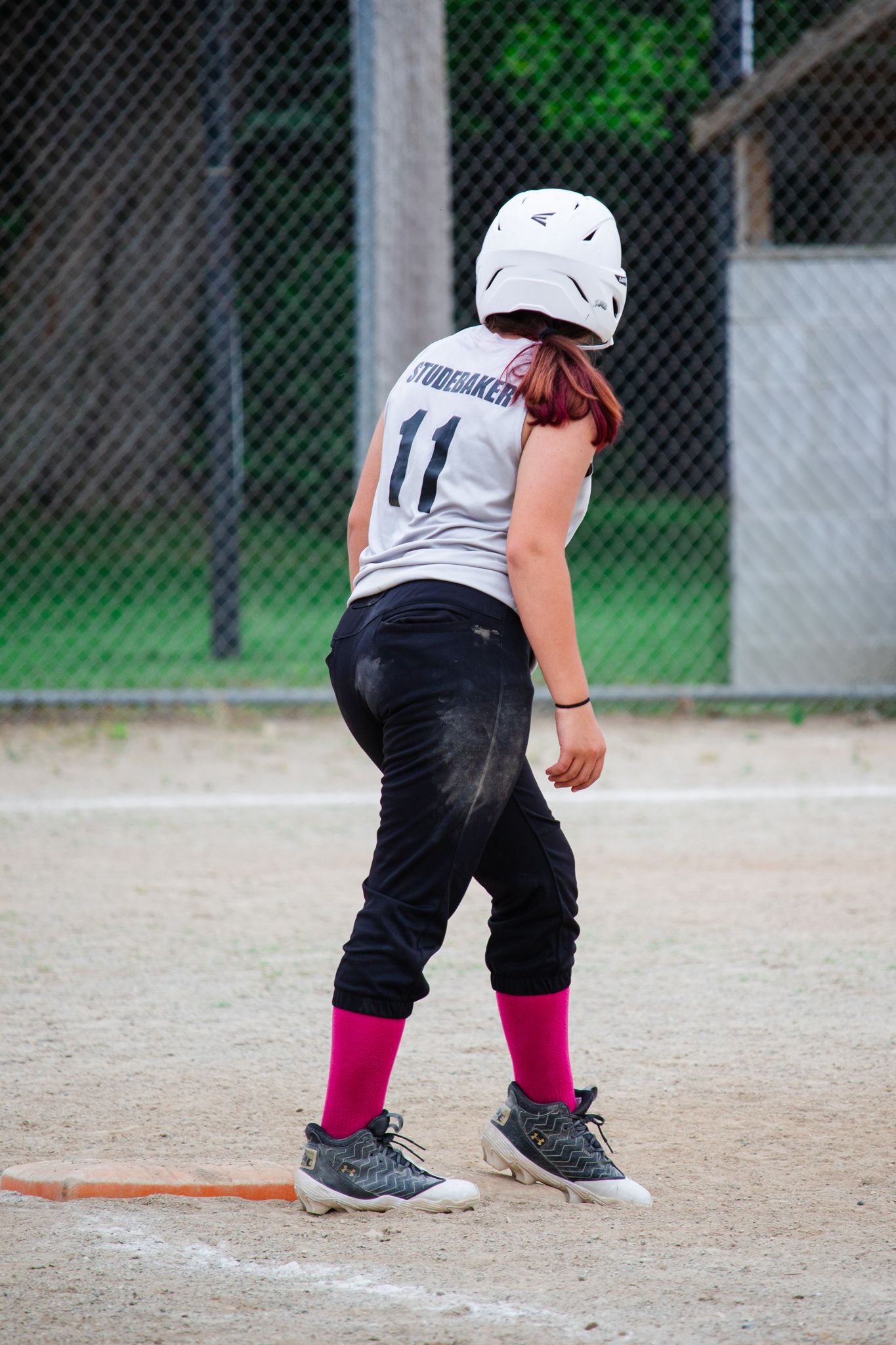 Close-up of softball player's legs and cleats near home plate wearing black pants and pink socks.