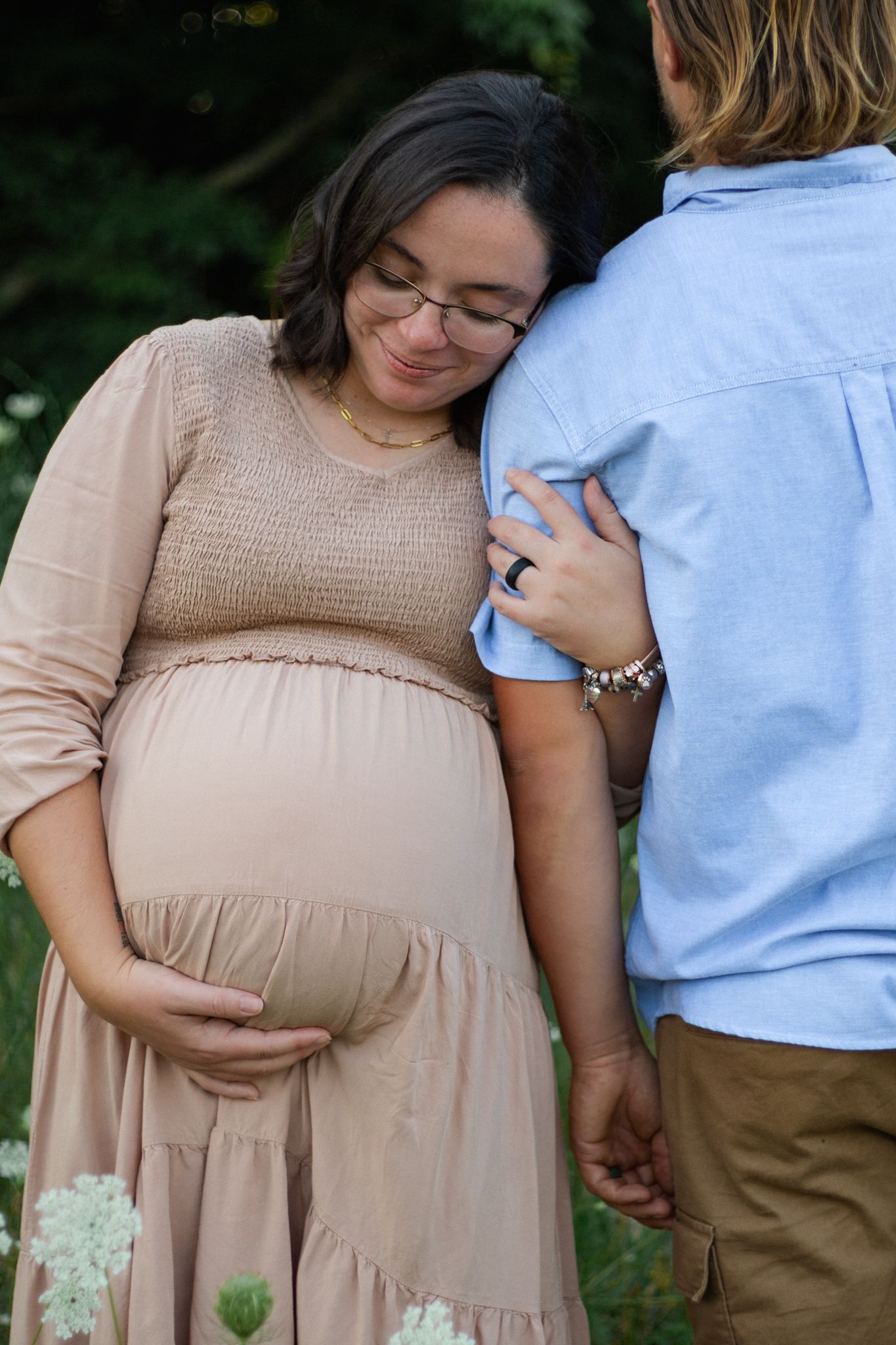 Intimate maternity portraits in a flowery field wearing beige dress.
