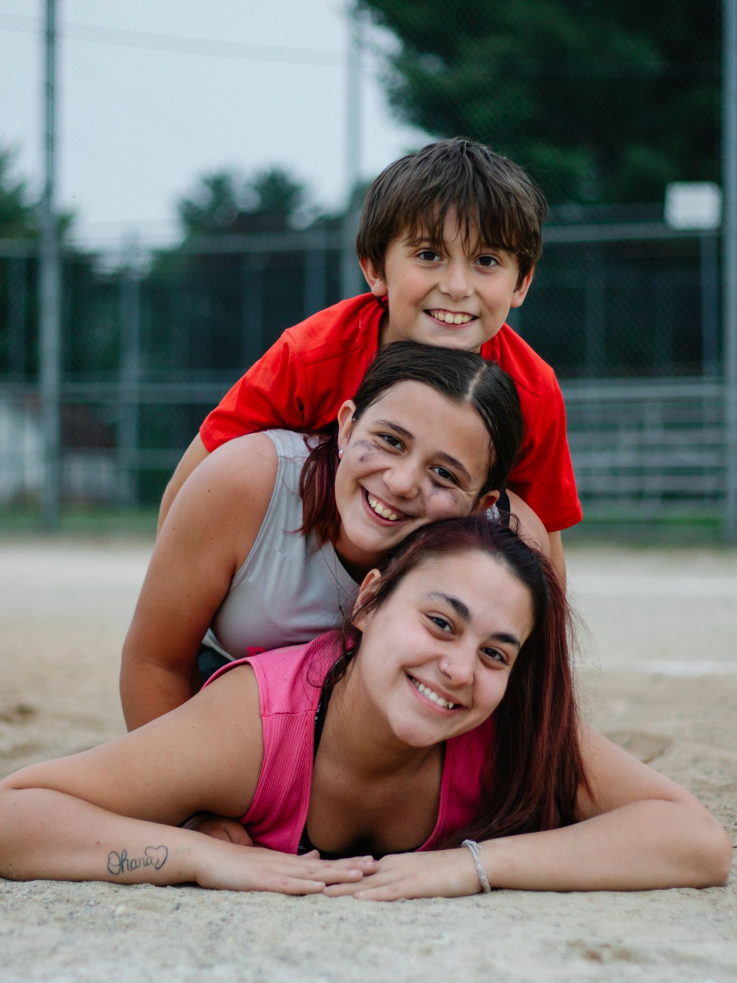 Playful pair lying in sand at baseball field showing joyful expressions.