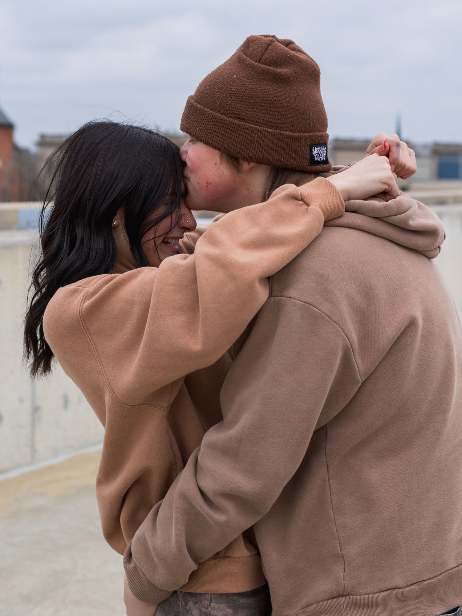 Intimate couple embrace in matching beige sweaters on an urban rooftop.