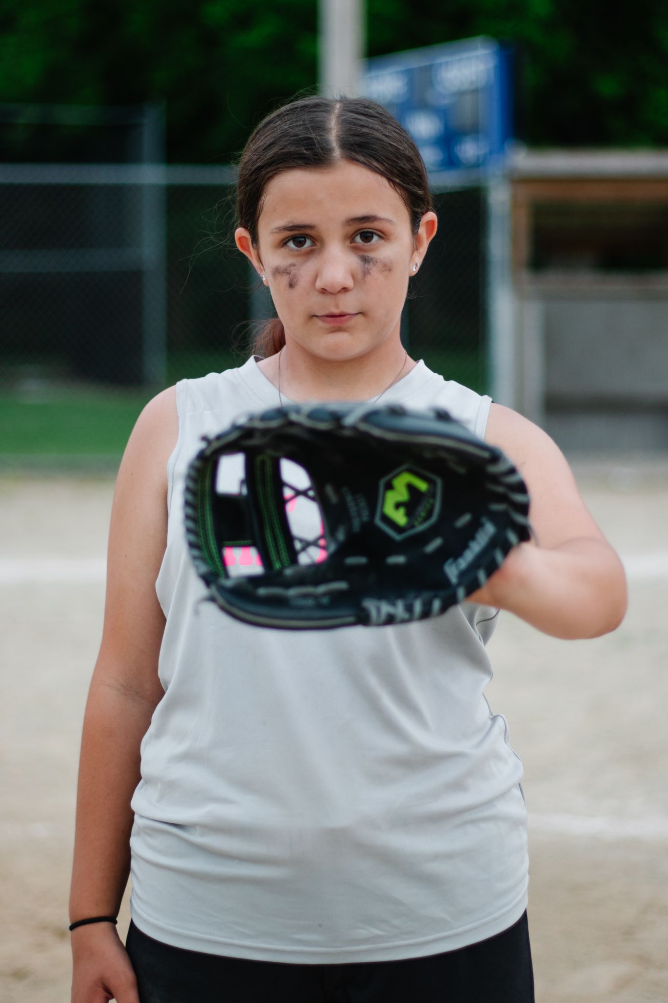 Player holds black softball glove while standing on baseball field.