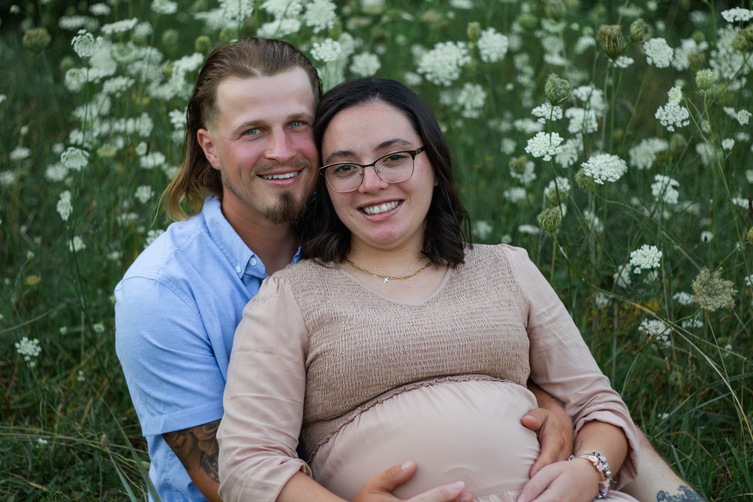 Expectant couple sitting together in a blooming wildflower meadow.