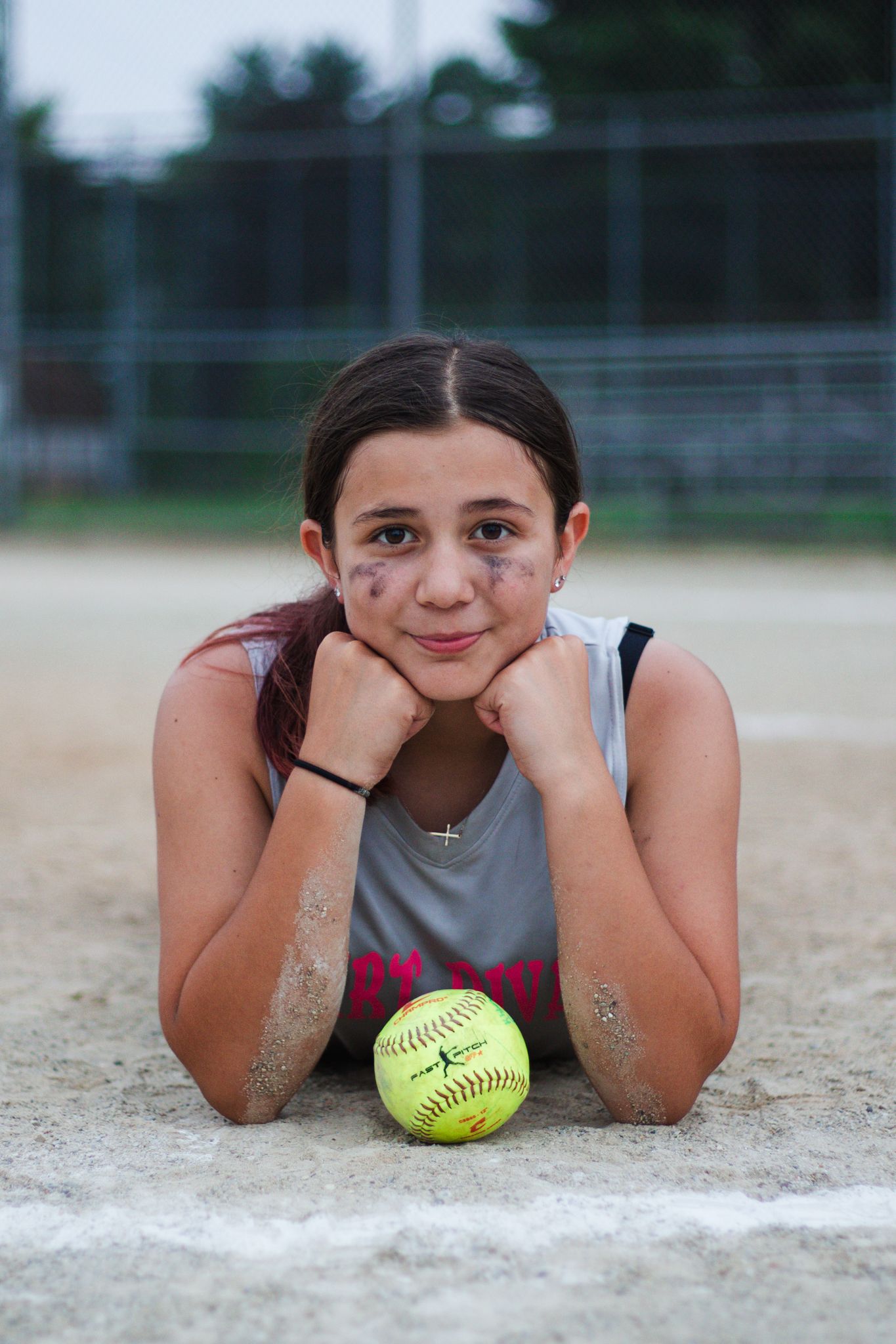 Player lies on baseball diamond chalk line with yellow softball.