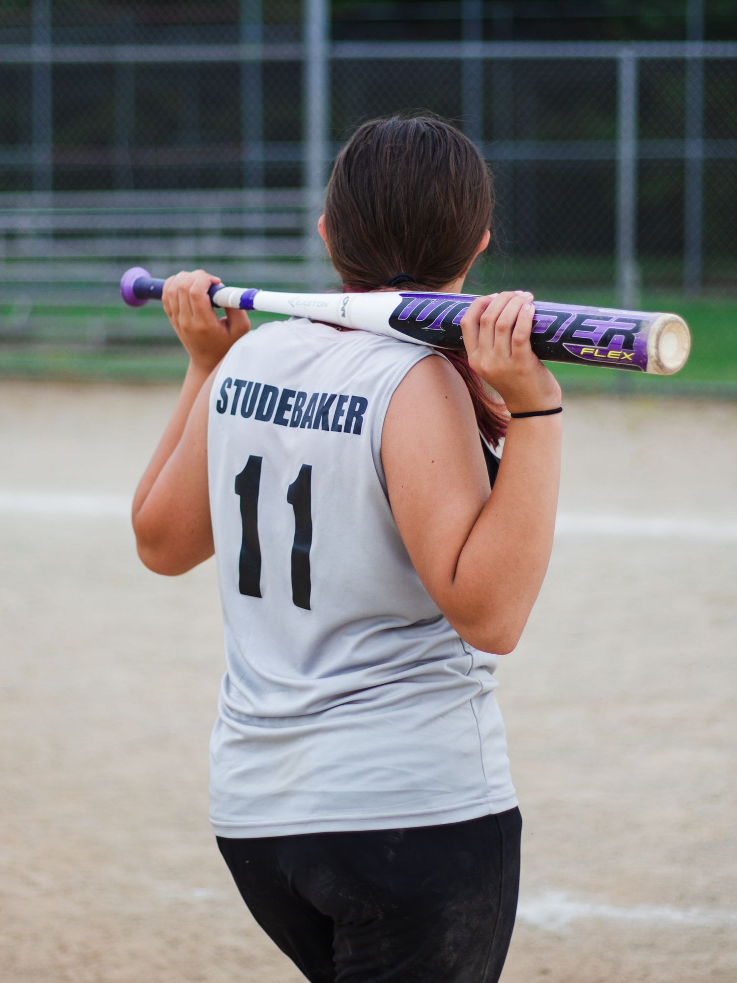 Back view of player wearing jersey number 11 holding a baseball bat on dirt field.