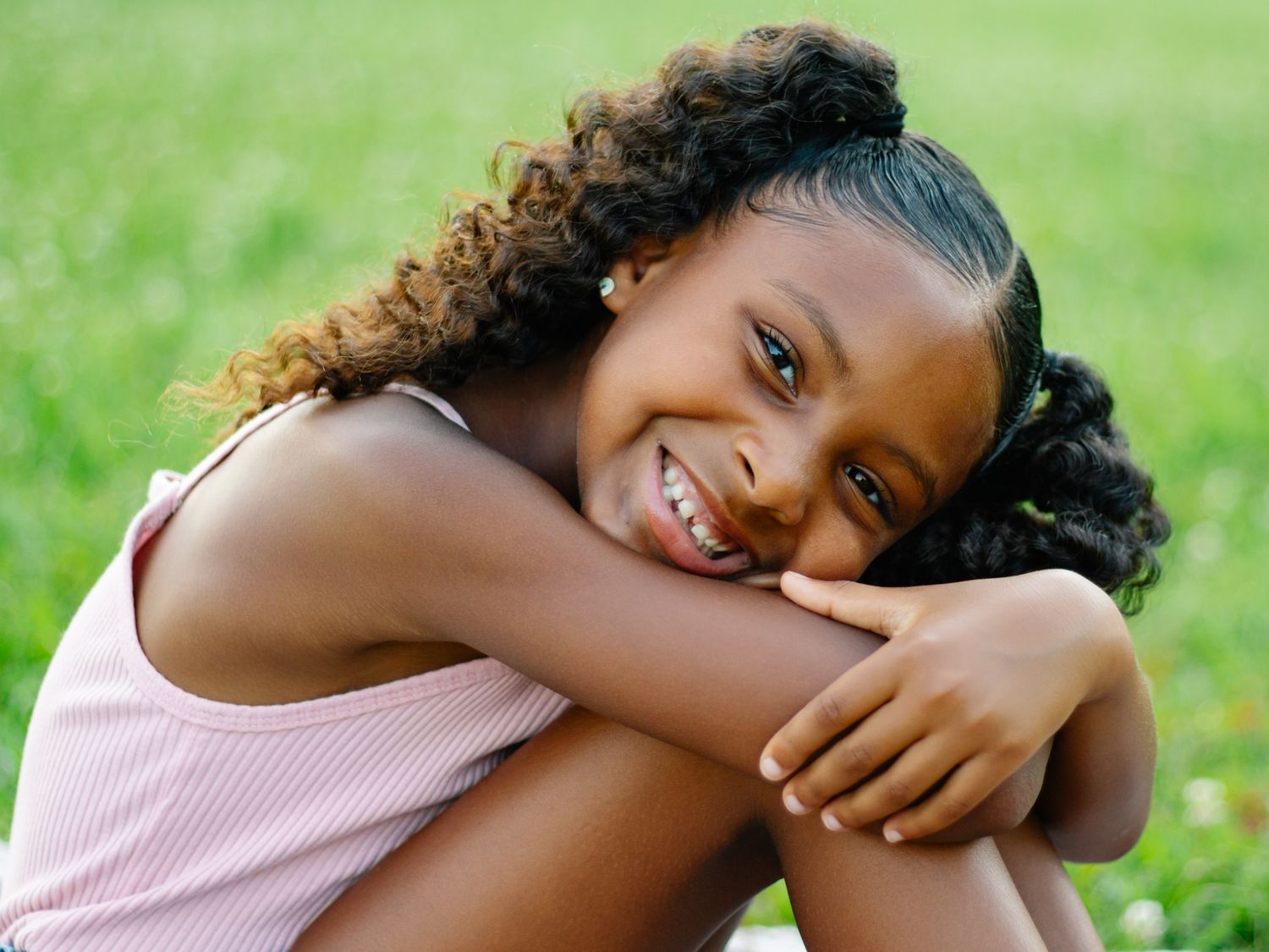 Child lounging on grey blanket in grass wearing pink top and denim outfit.