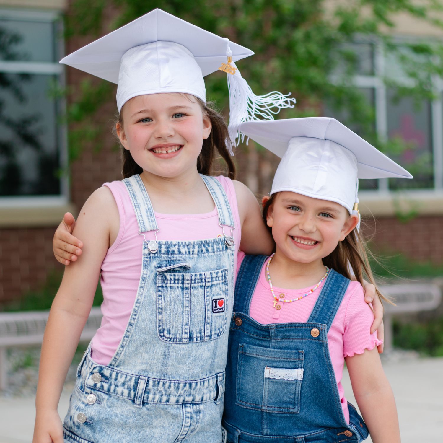 Graduates wearing denim overalls and white caps pose together outdoors.